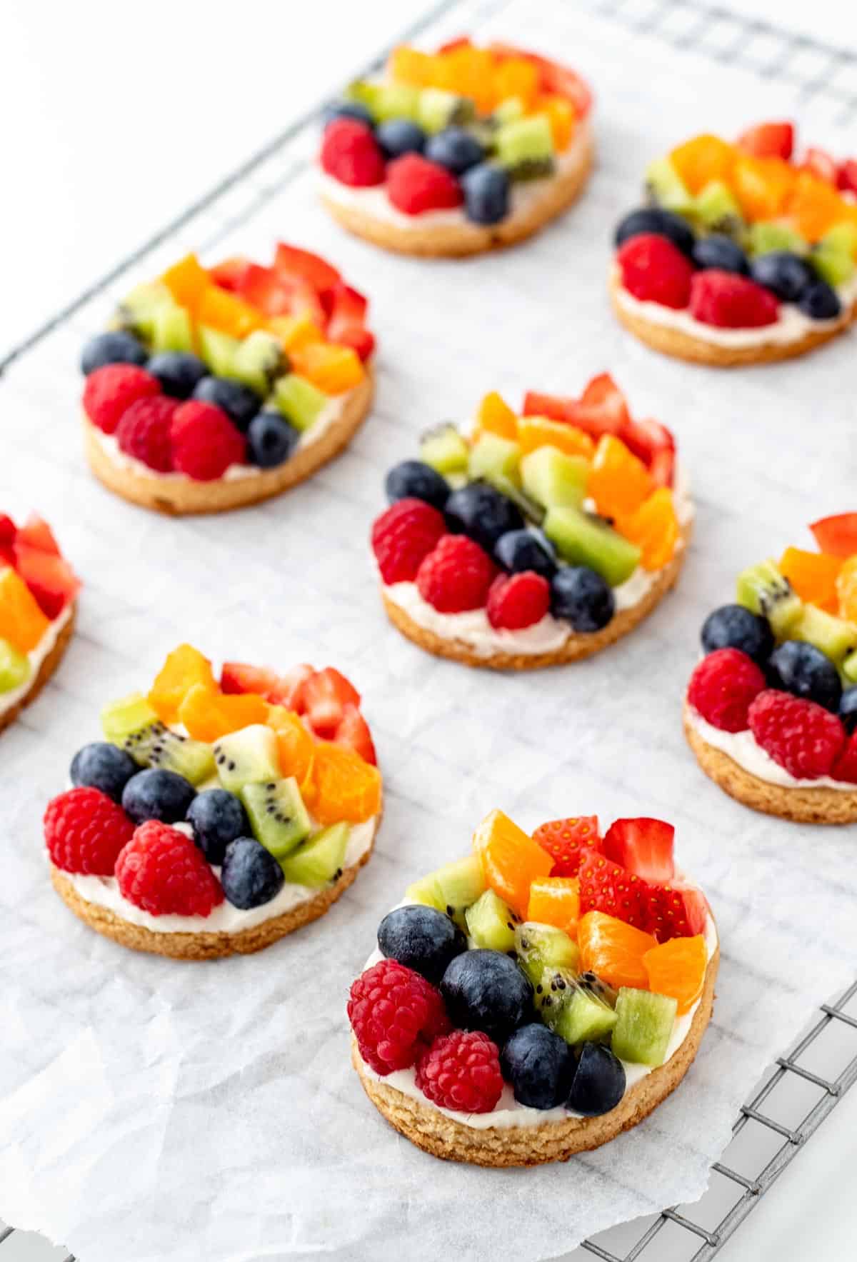 Mini fruit pizzas in the shape of an Easter egg on a cooling rack lined with parchment paper.