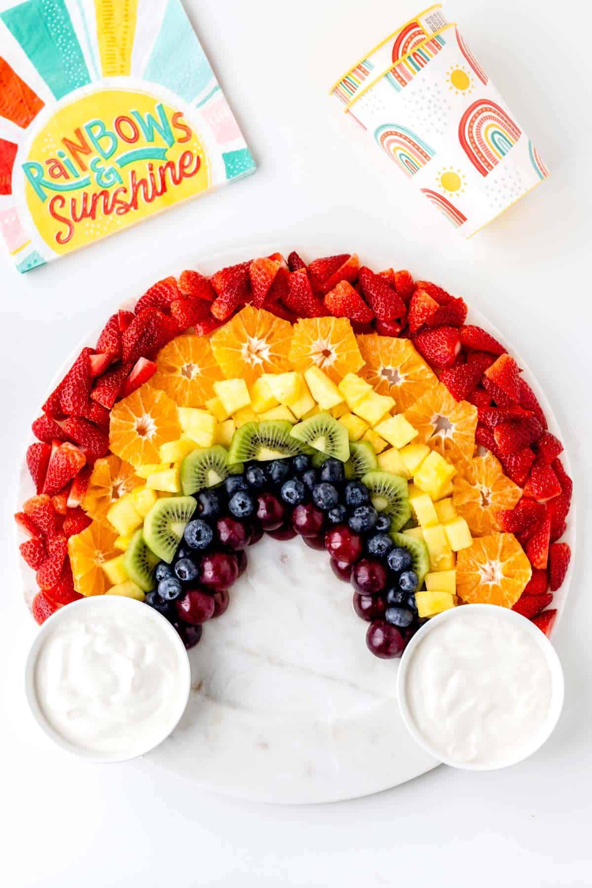 Rainbow fruit board on a decorative platter with yogurt dip on each end.