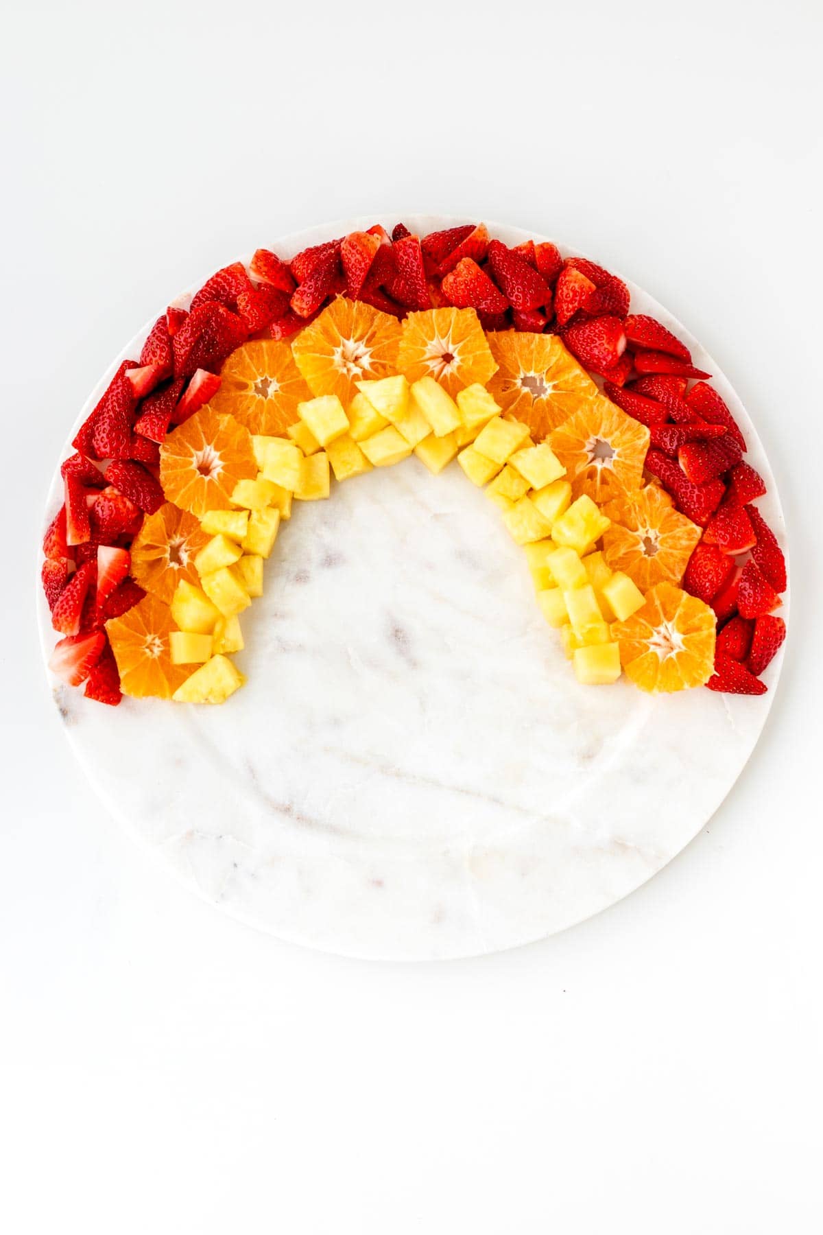 The strawberries, oranges, and pineapple arranged in the shape of a rainbow for the rainbow fruit tray.