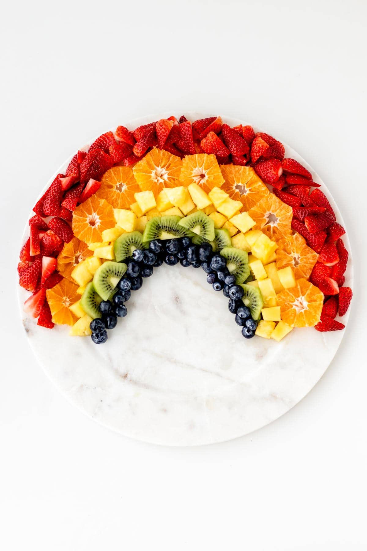 Strawberries, oranges, pineapple, kiwi, and blueberries arranged into the shape of a rainbow.