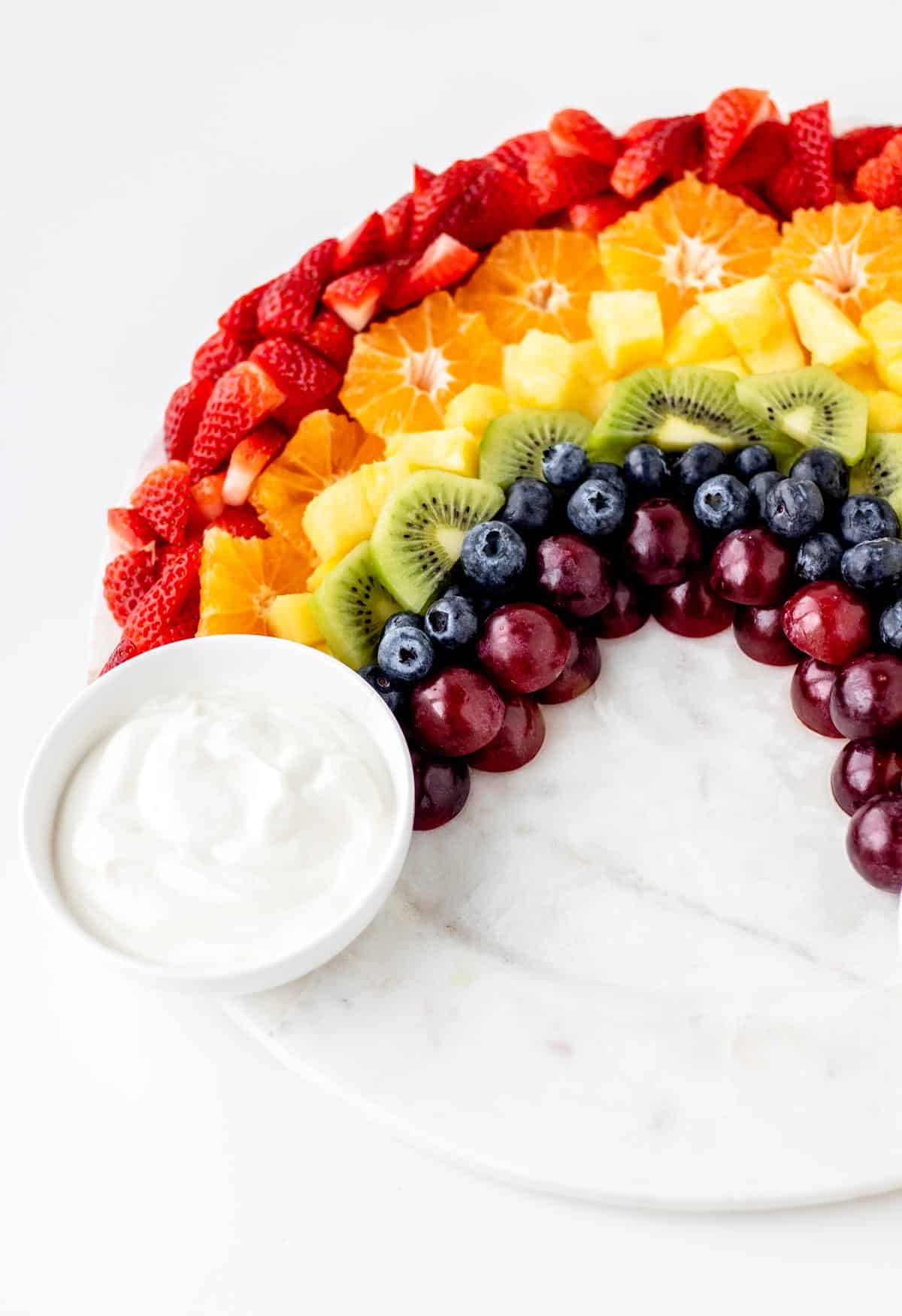 One side of the rainbow fruit tray assembled with a small bowl of vanilla yogurt dip at the base to resemble a cloud.
