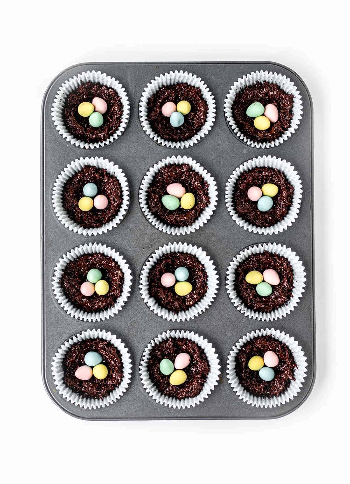 A muffin tin with 12 shredded wheat Easter nests.