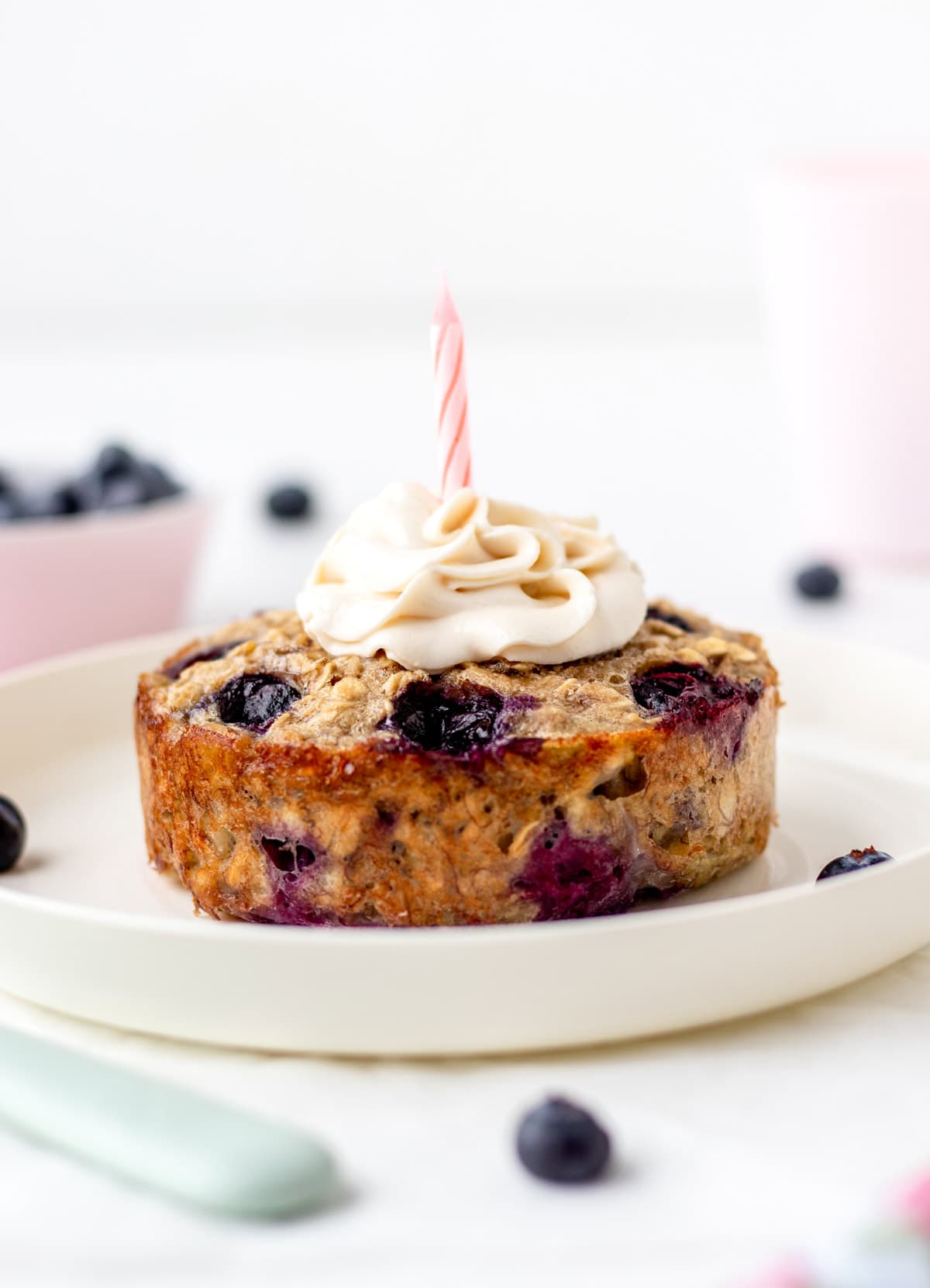 Single serving of baked oatmeal on a white plate with a small dollop of cream cheese frosting and candle on top.