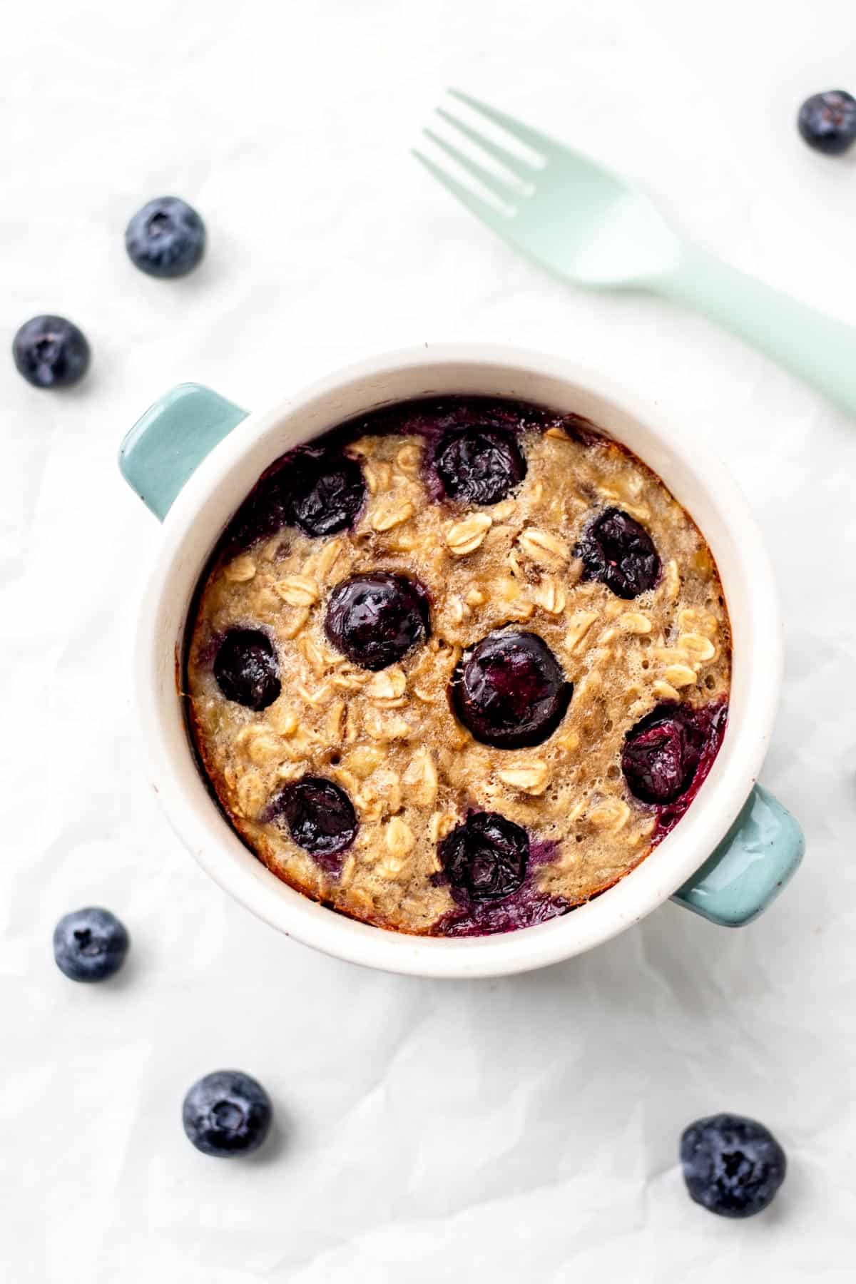 Baked oats for one in a ramekin surrounded by blueberries and a fork.