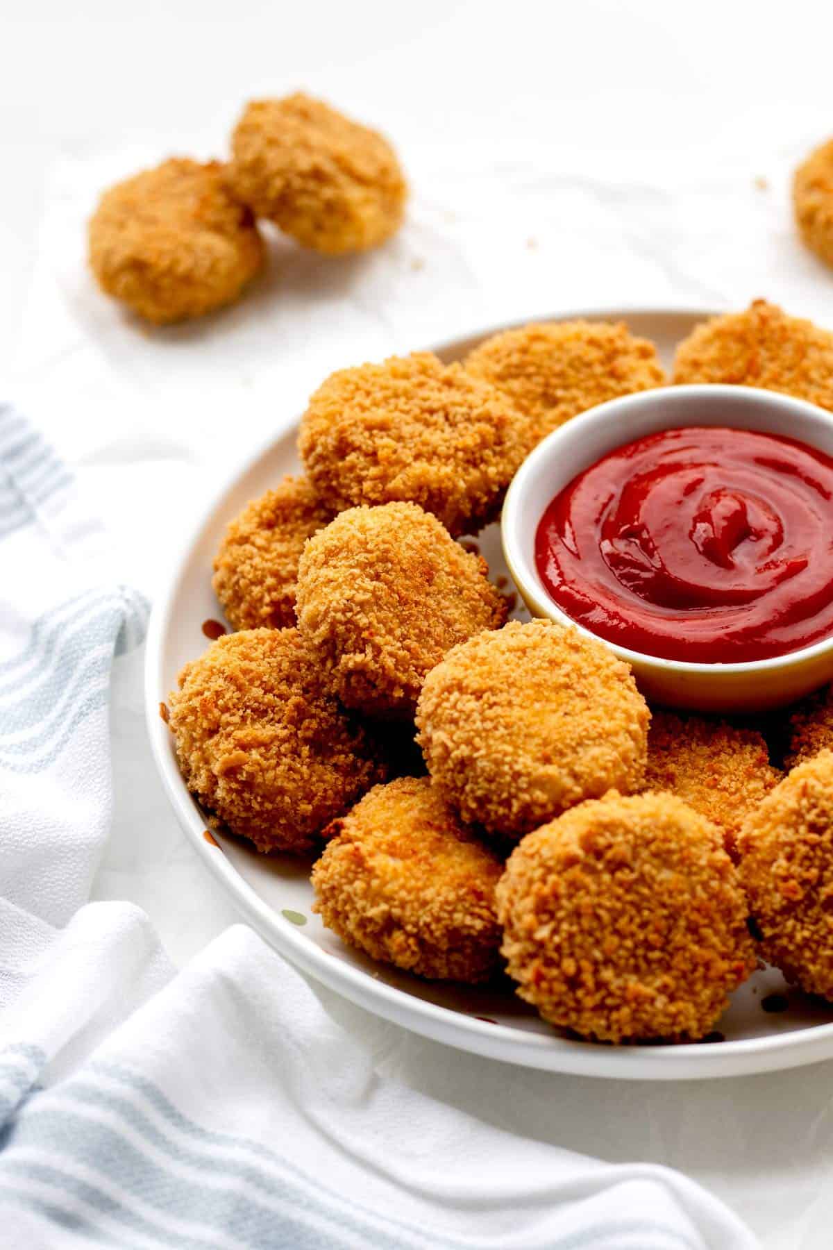 Cauliflower chicken nuggets arranged on a circular platter with a bowl of ketchup in the middle.