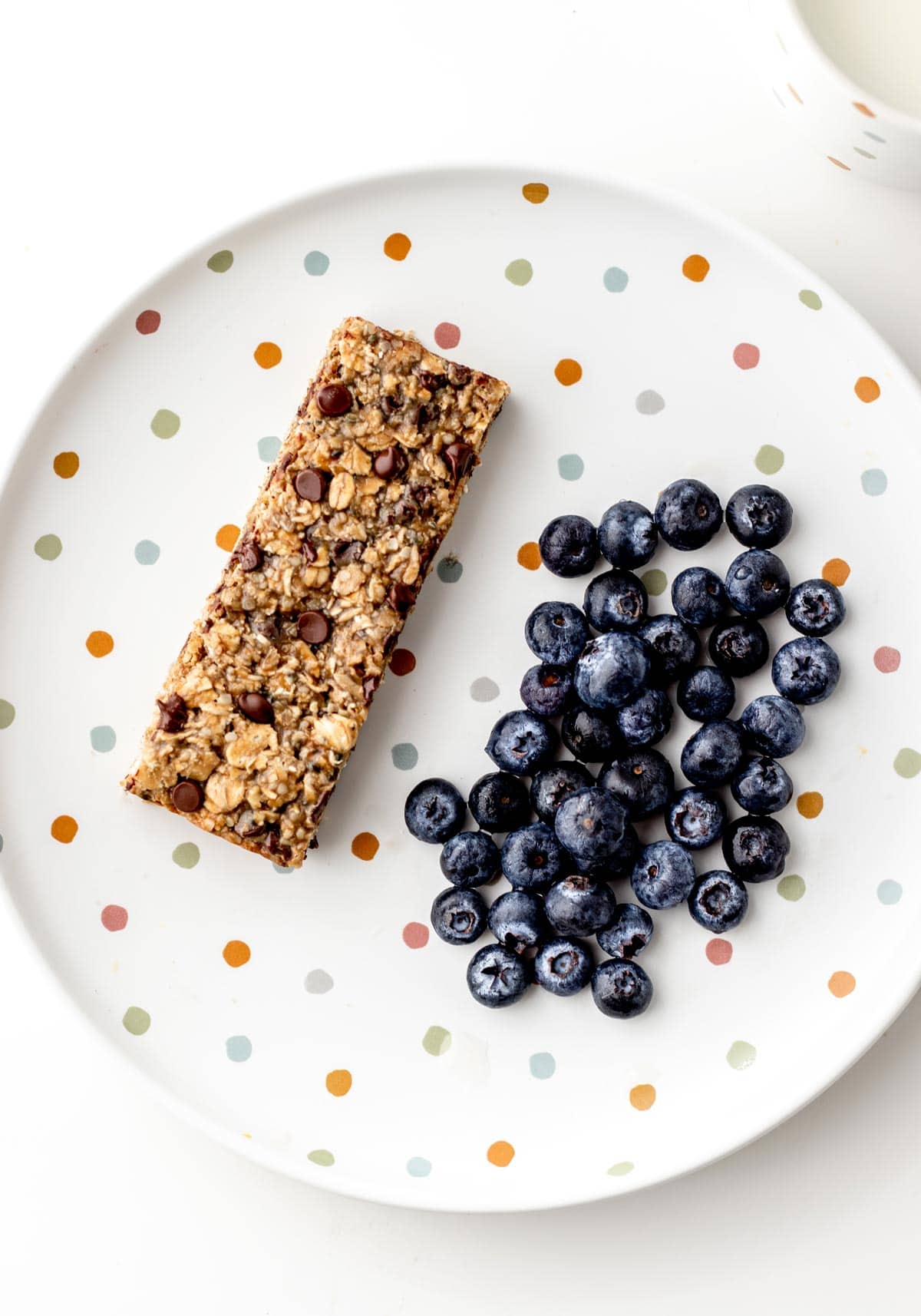 A nut free breakfast bar and a handful of blueberries on a polka dotted plate.