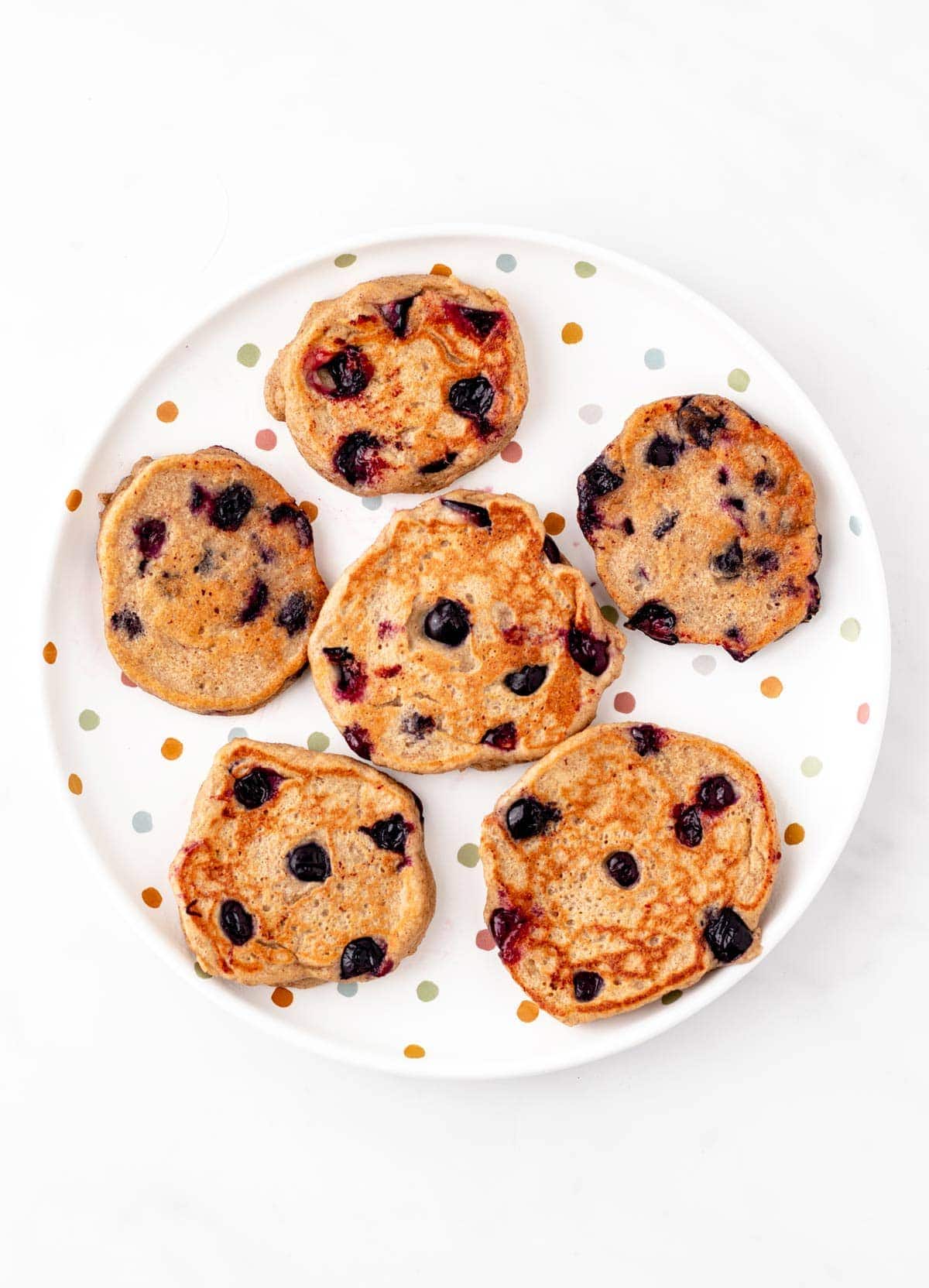 6 mini blueberry pancakes spread out on a polka dotted plate.