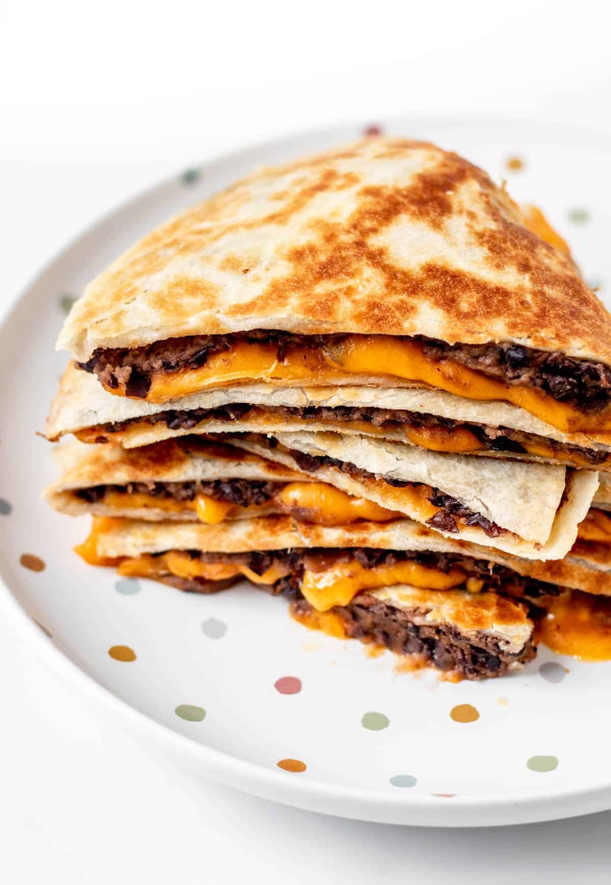 Baby led weaning quesadillas quartered and stacked on top of each other on a polka dot plate.