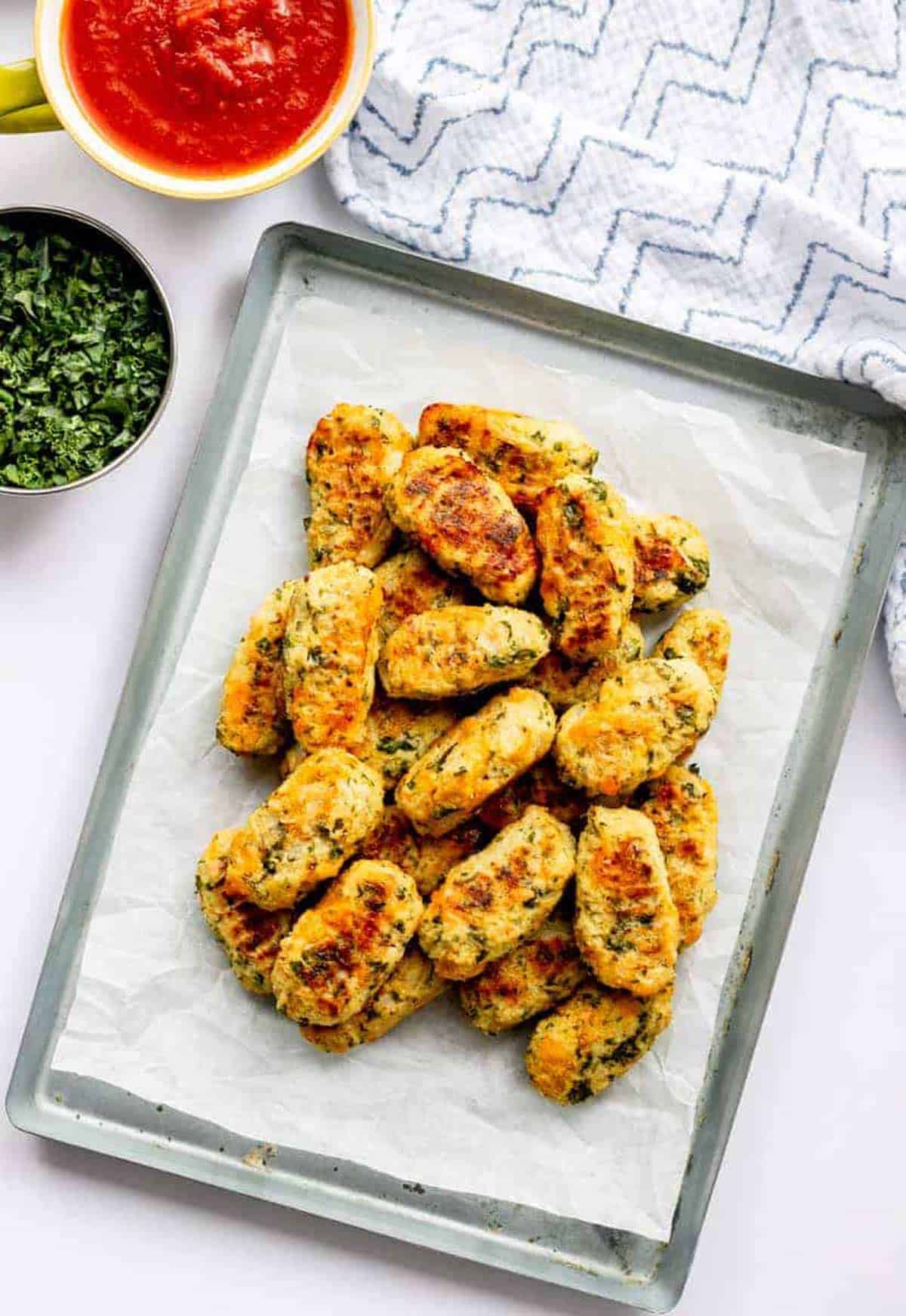 Baked cauliflower tots on a parchment paper lined baking sheet.