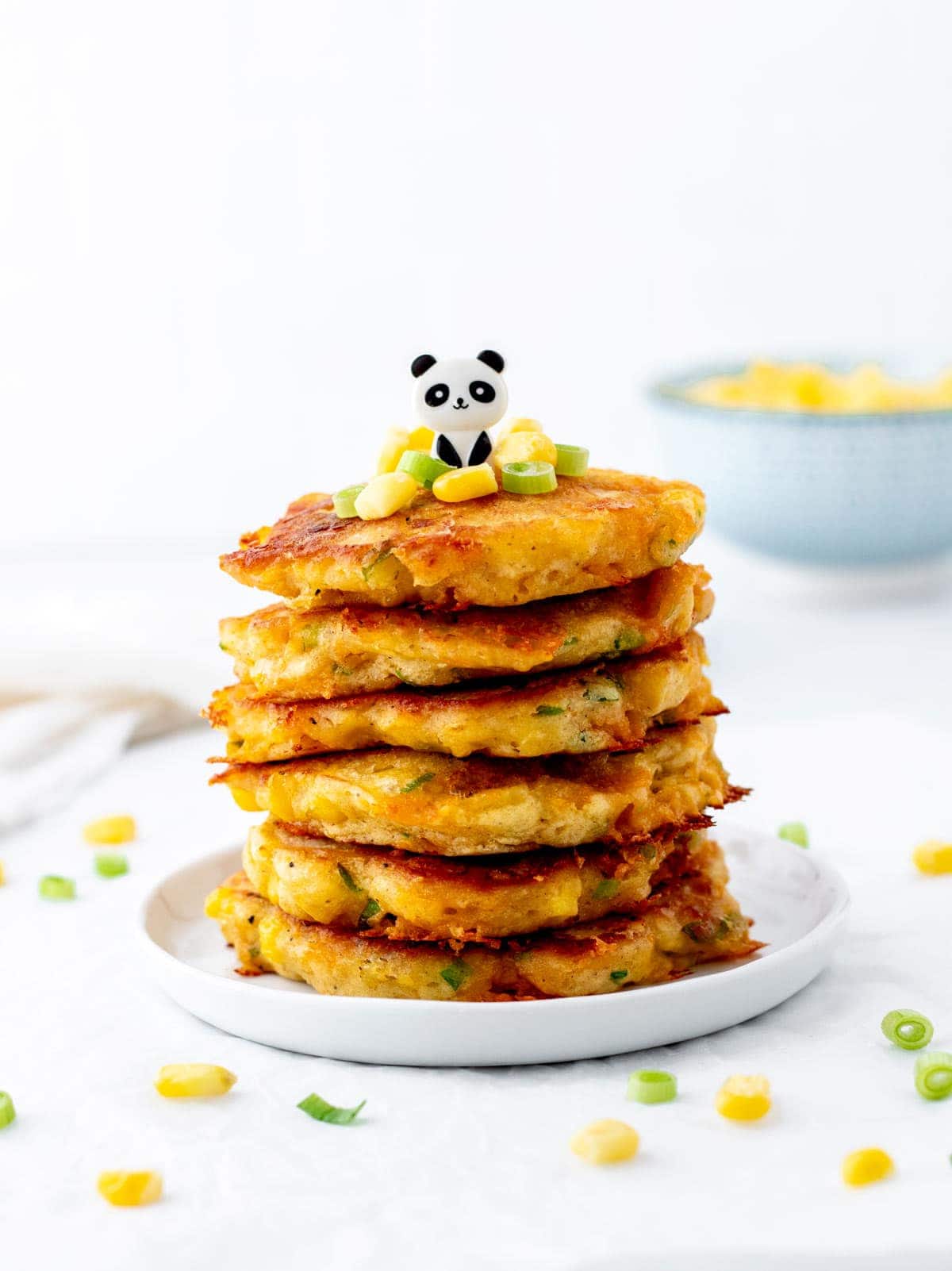 Corn fritters stacked on top of one another on a small white plate with a decorative panda toothpick on top.