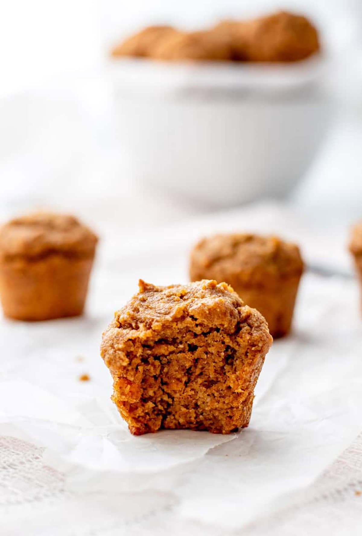 A mini sweet potato muffin with a bite taken out of it on a counter, with more muffins in the background.