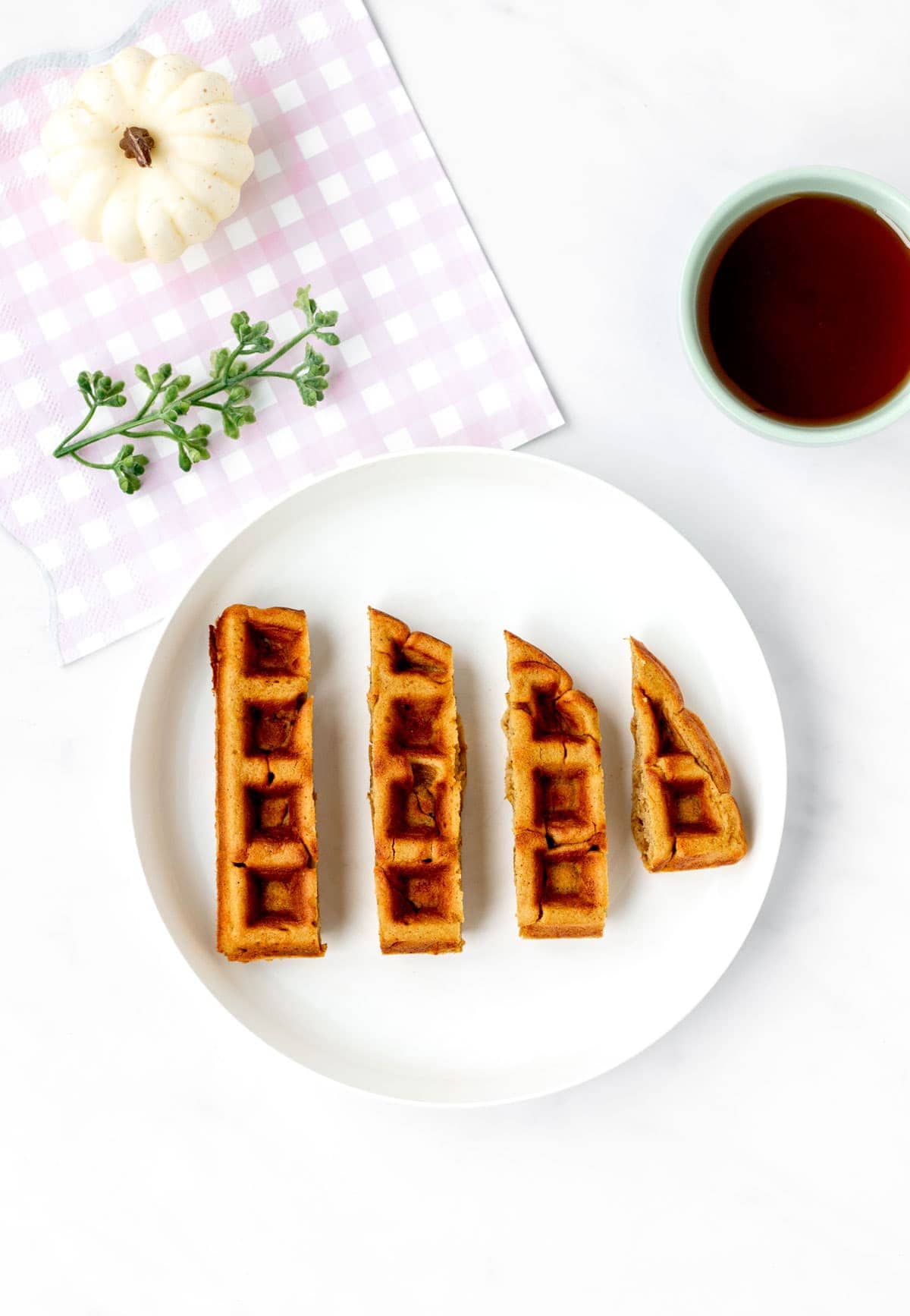 Pumpkin oat waffles cut into finger-like strips on a white plate next to a small bowl of syrup.