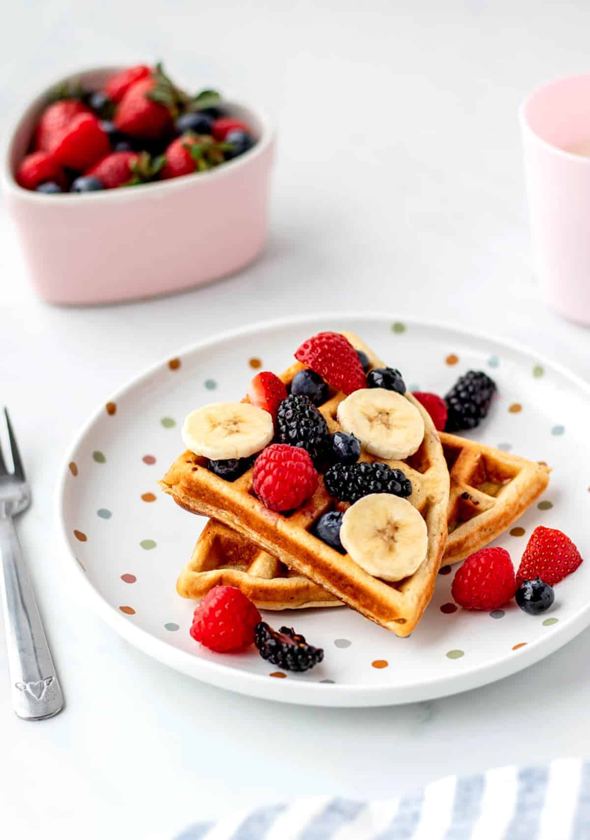 Two slices of 3-ingredient protein waffles stacked on top of one another on a polka dot plate.