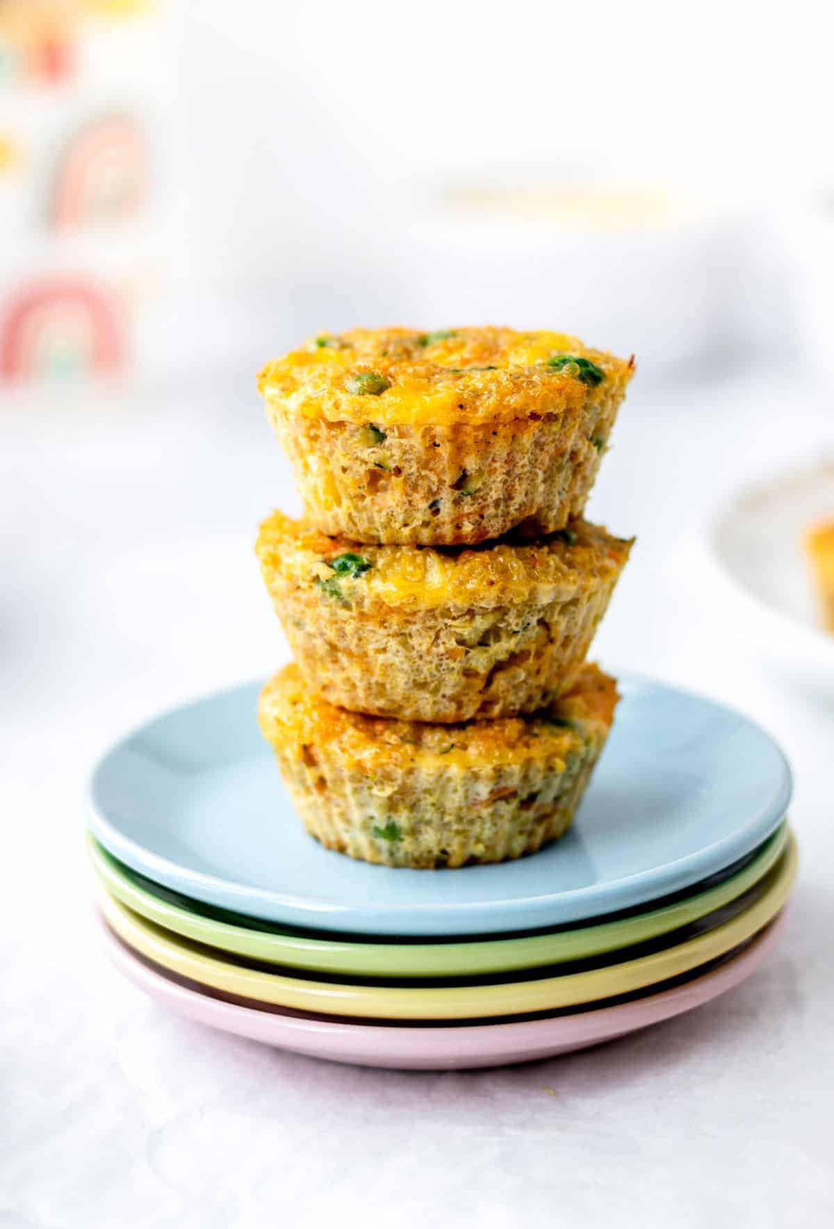 3 baked veggie quinoa bites stacked on top of one another on a stack of colorful plates.