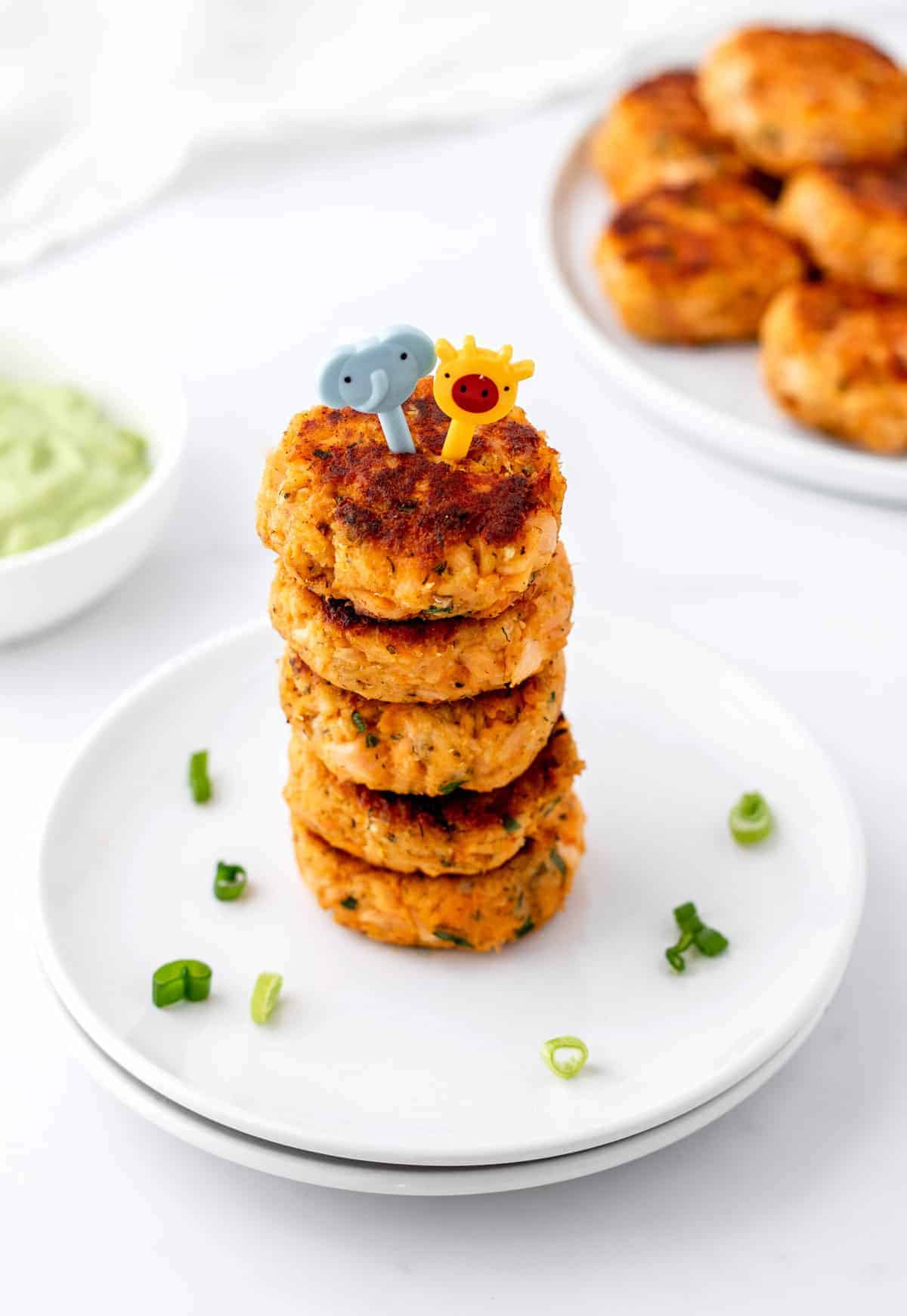 Mini salmon cakes stacked on top of one another on a white plate.