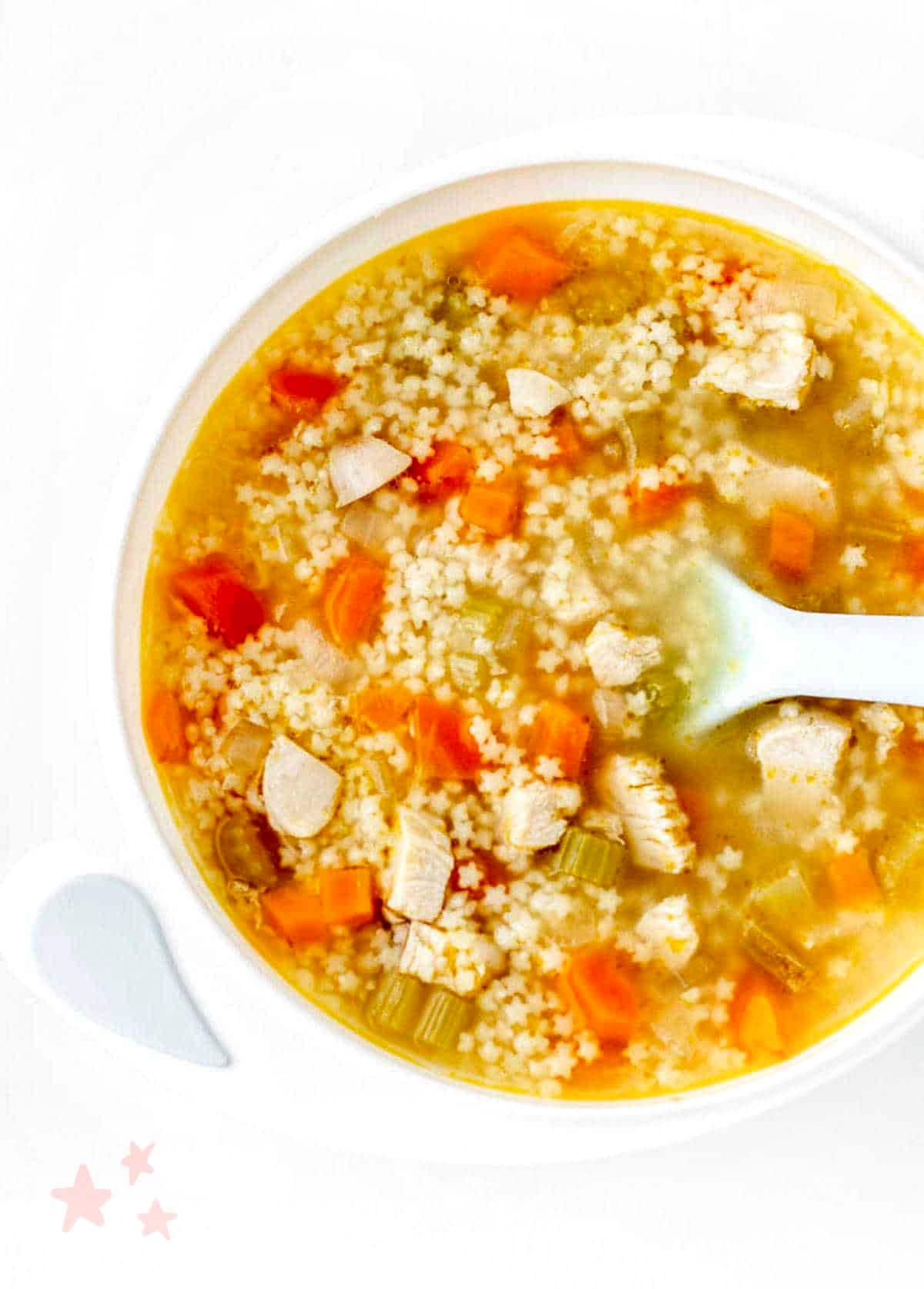 Chicken pastina soup in a white bowl with a spoon.