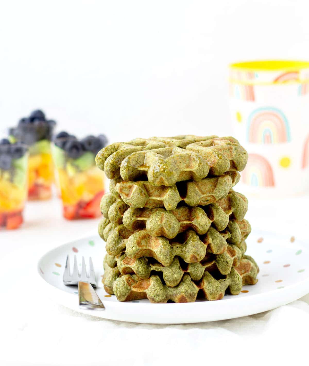 Spinach banana waffles stacked on top of one another on a white plate.