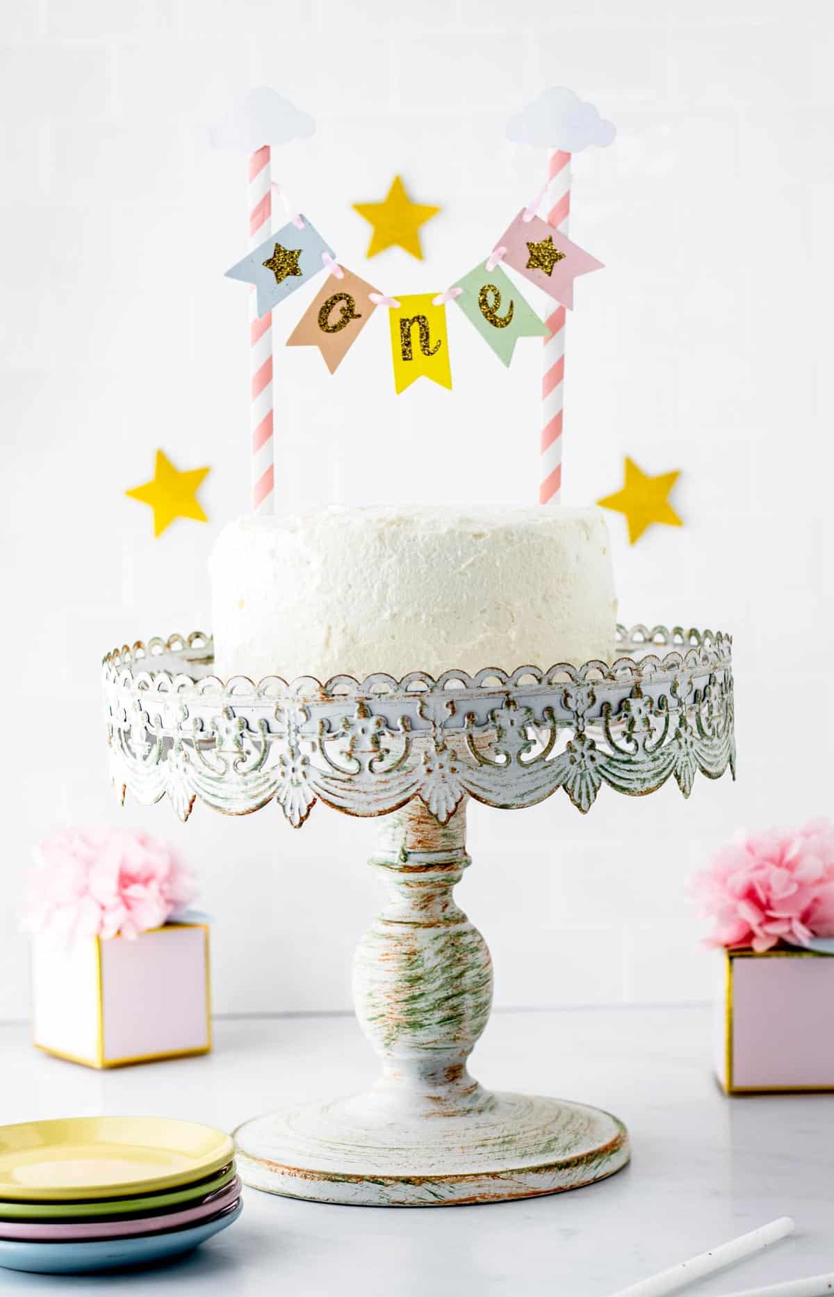 A healthy smash cake with two candles in it on a cake tower on a table.