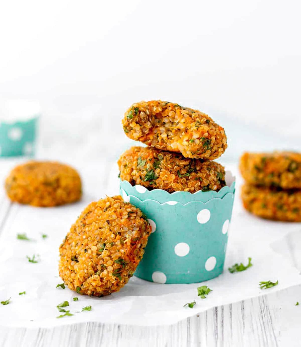 Sweet potato quinoa cakes stacked on top of one another in a polka dotted paper cup on a white plate.