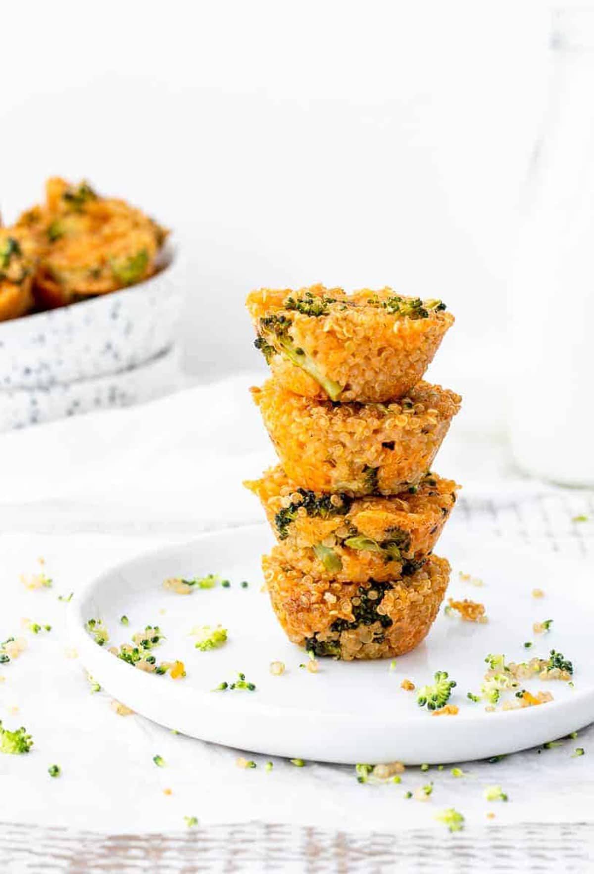 Broccoli cheddar quinoa bites stack on top of one another on a white plate.