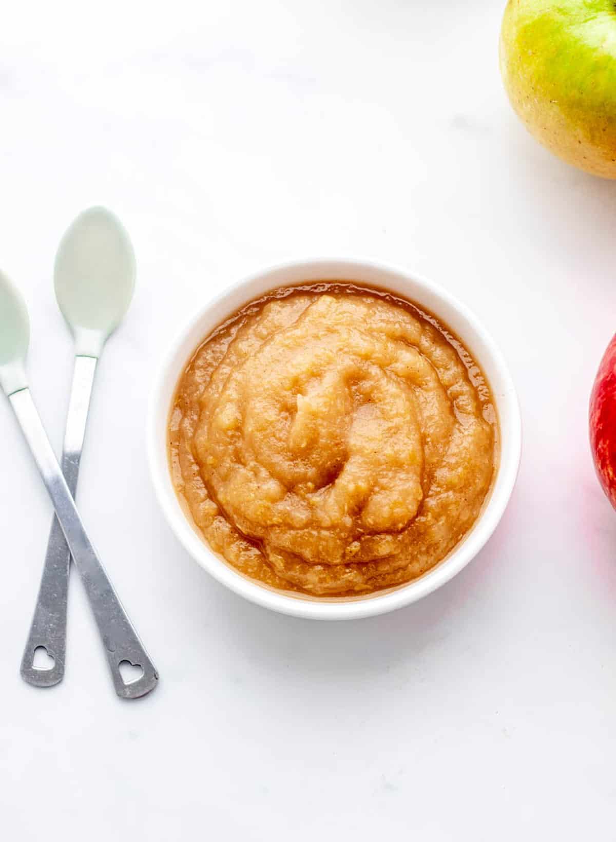 A small bowl of unsweetened applesauce next to spoons.