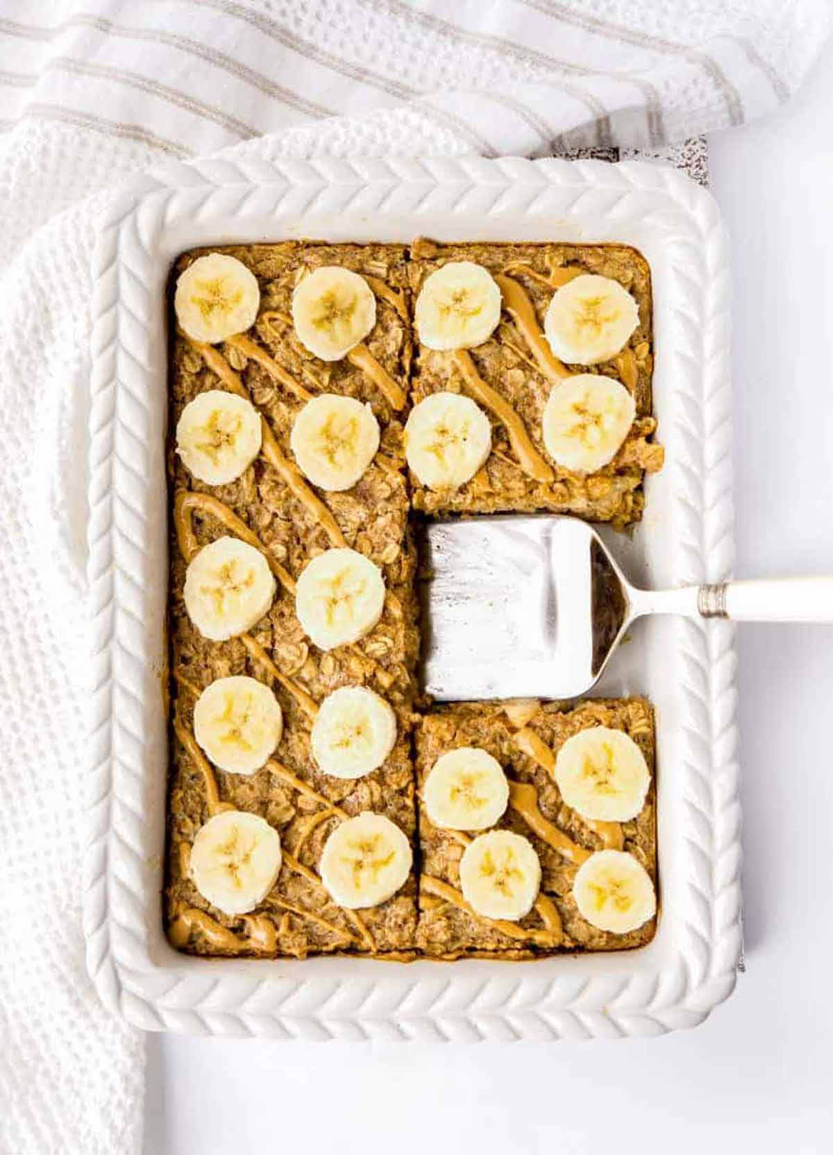 A baking dish with peanut butter banana baked oatmeal with a spatula scooping out a piece.