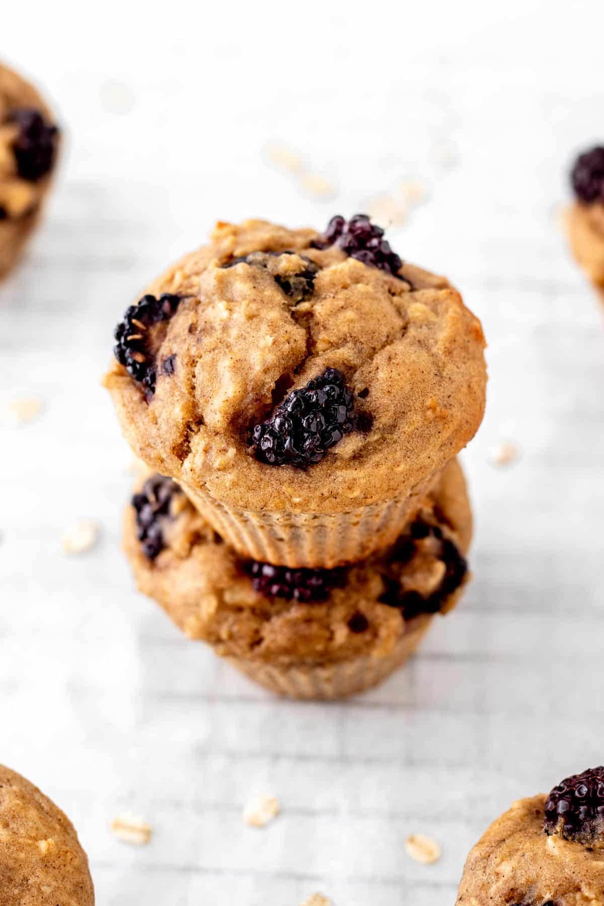 Two blackberry oatmeal muffins stacked on top of one another on a cooling rack.