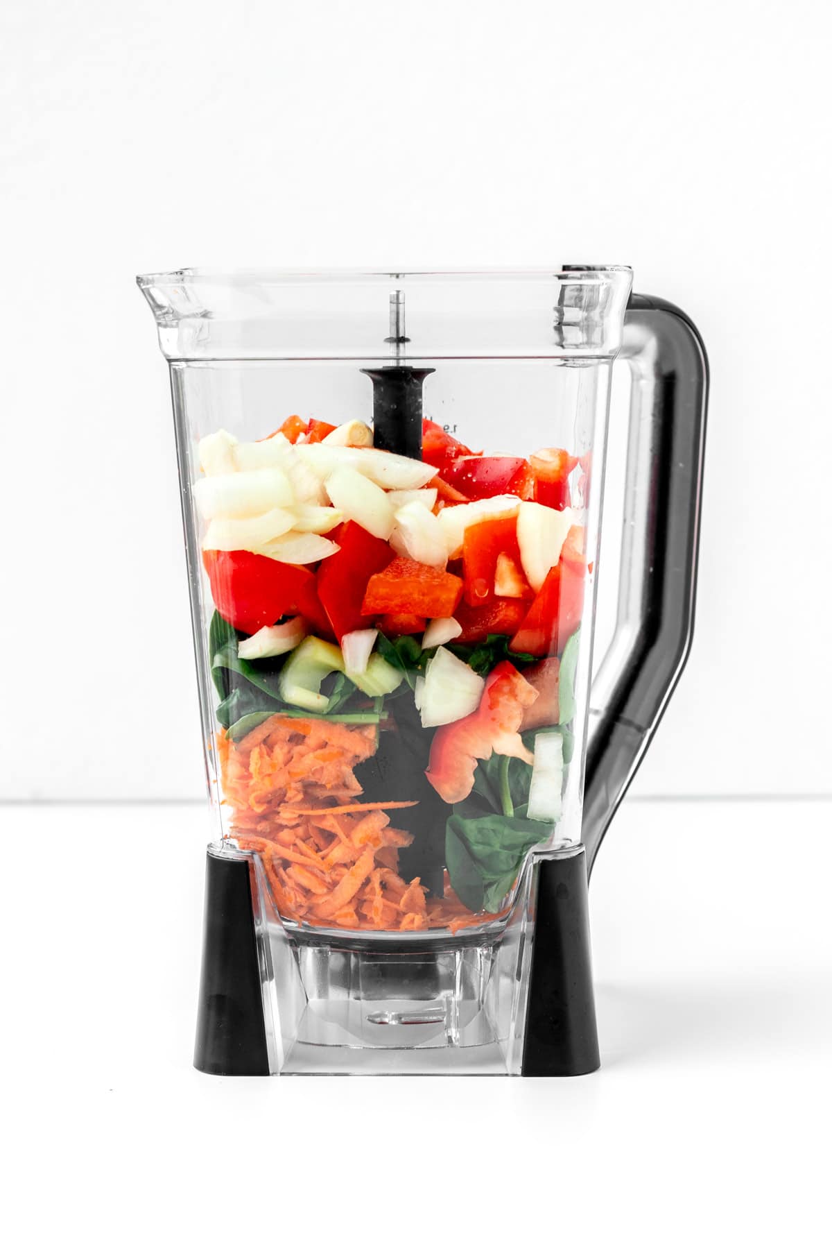 Different vegetables layered in a blender.