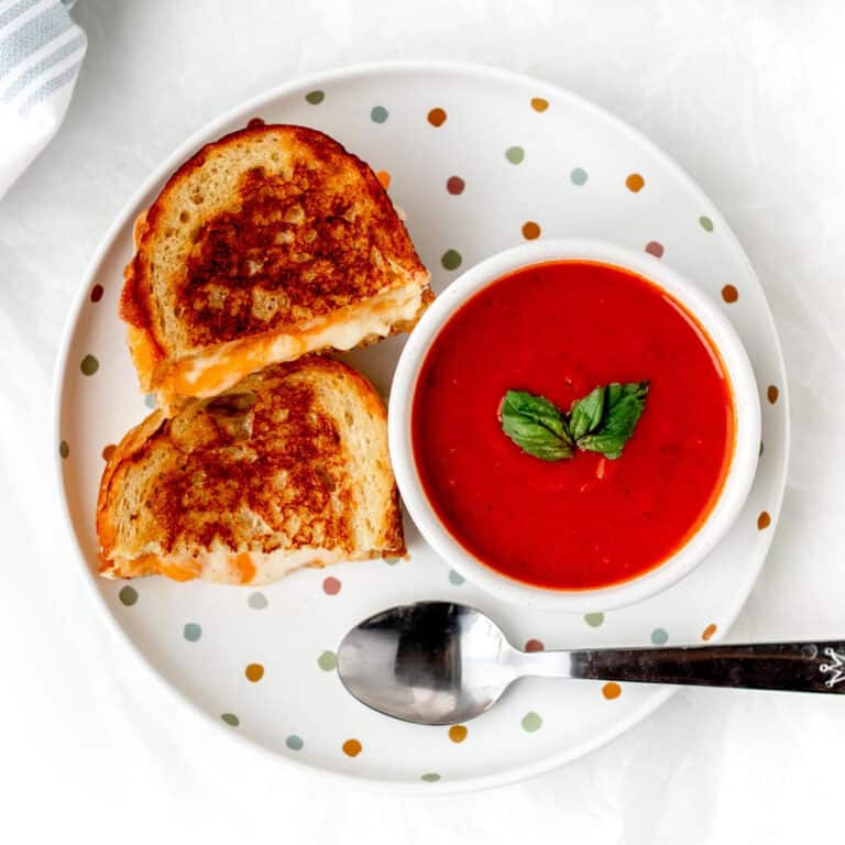 Grilled cheese sandwich cut in half on a plate with a bowl of tomato basil soup.