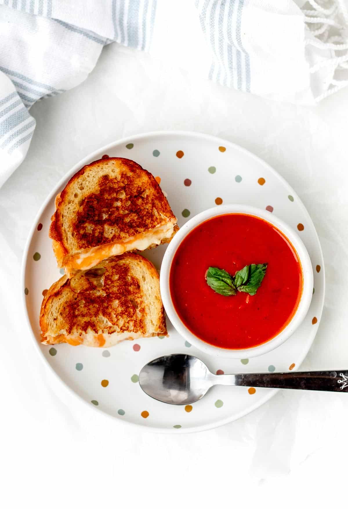 A birds-eye view of a grilled cheese sandwich and cup of tomato soup on a polka dotted plate.