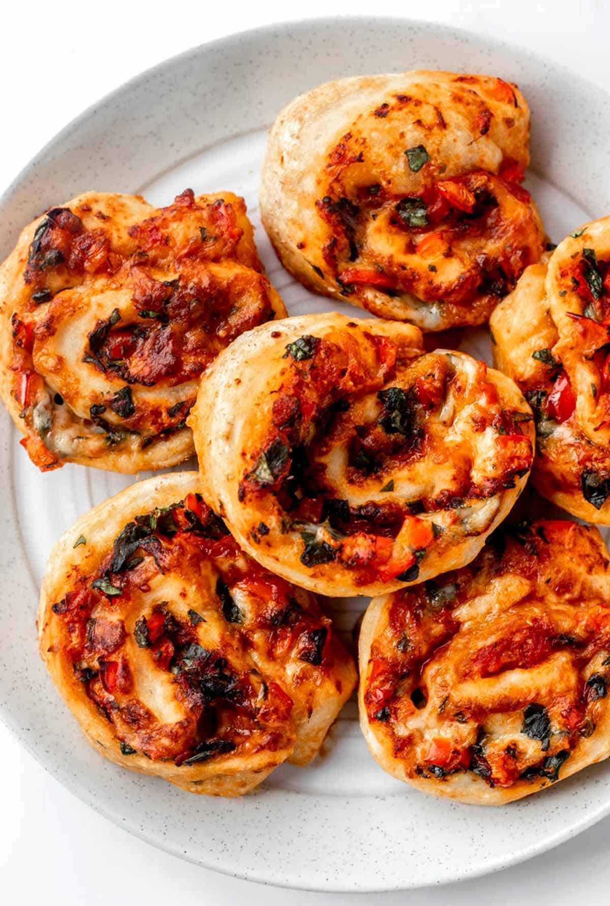 Homemade pizza rolls stacked on top of one another on a white plate.