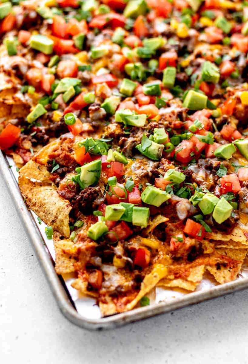 Beef nachos supreme on a baking sheet, topped with avocado slices.