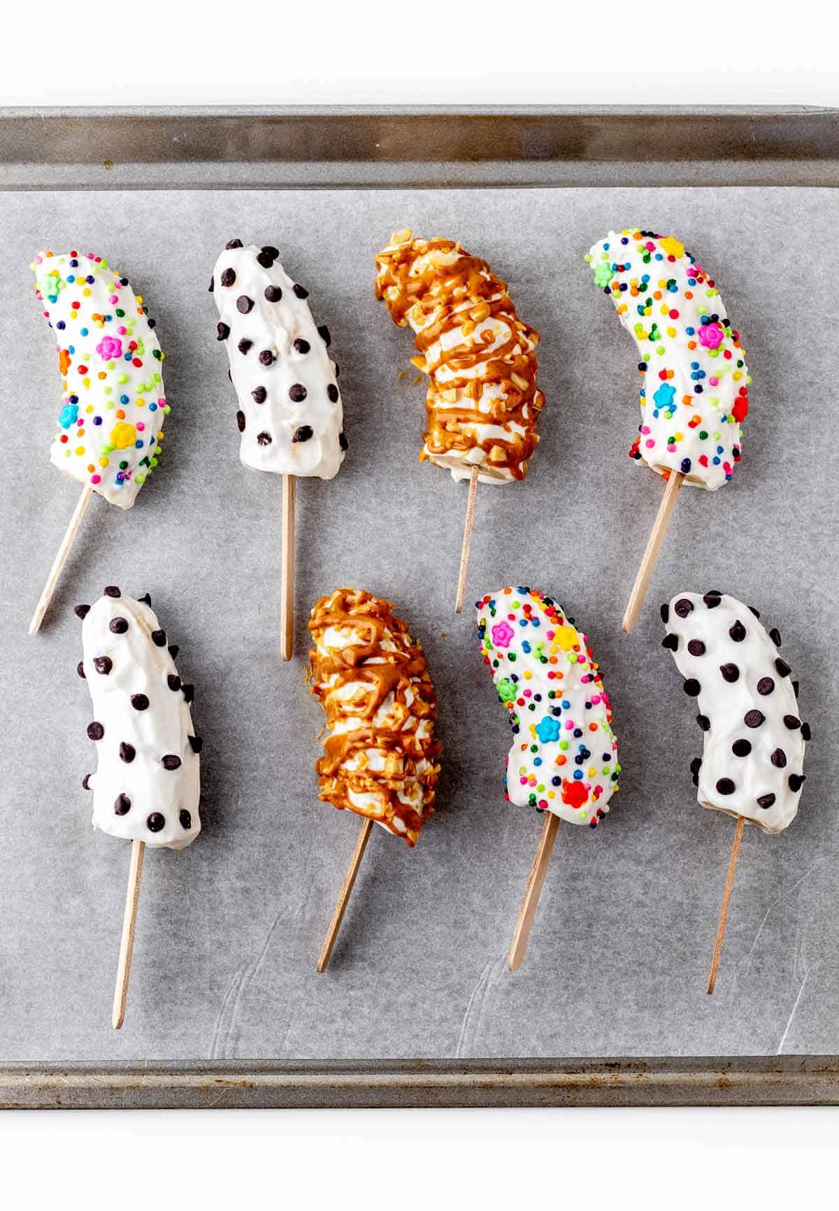 Frozen banana pops with yogurt decorated with sprinkles on a parchment paper lined baking sheet.