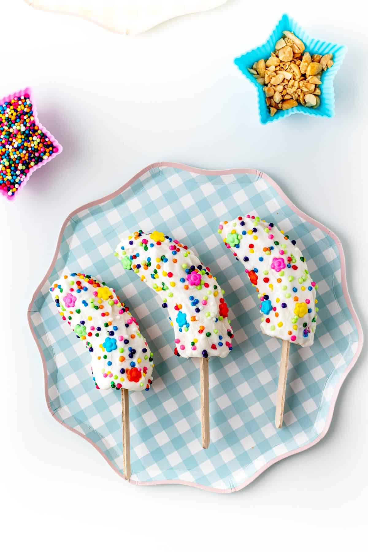 Frozen banana pops covered in Greek yogurt and sprinkles on a blue and white plaid plate.