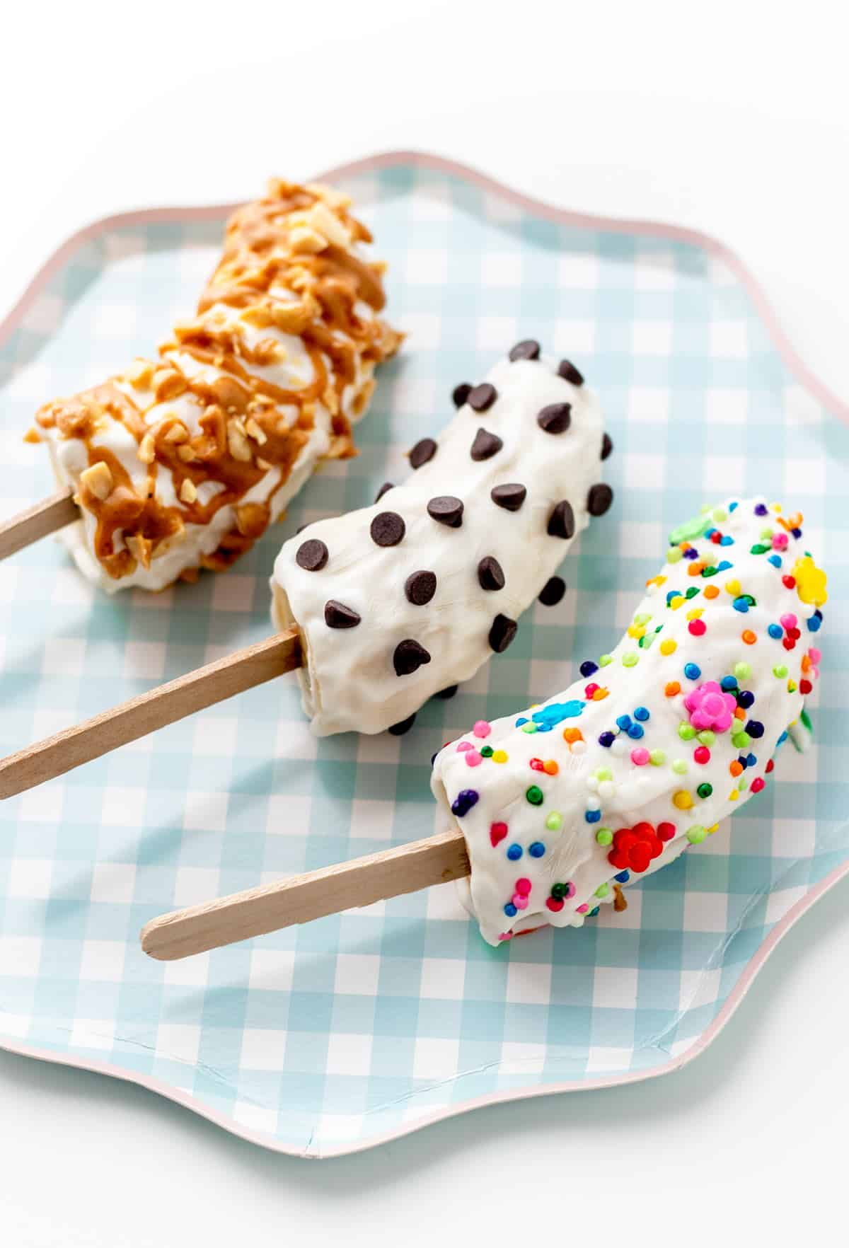 Decorated frozen banana pops with yogurt on a blue and white plaid plate.