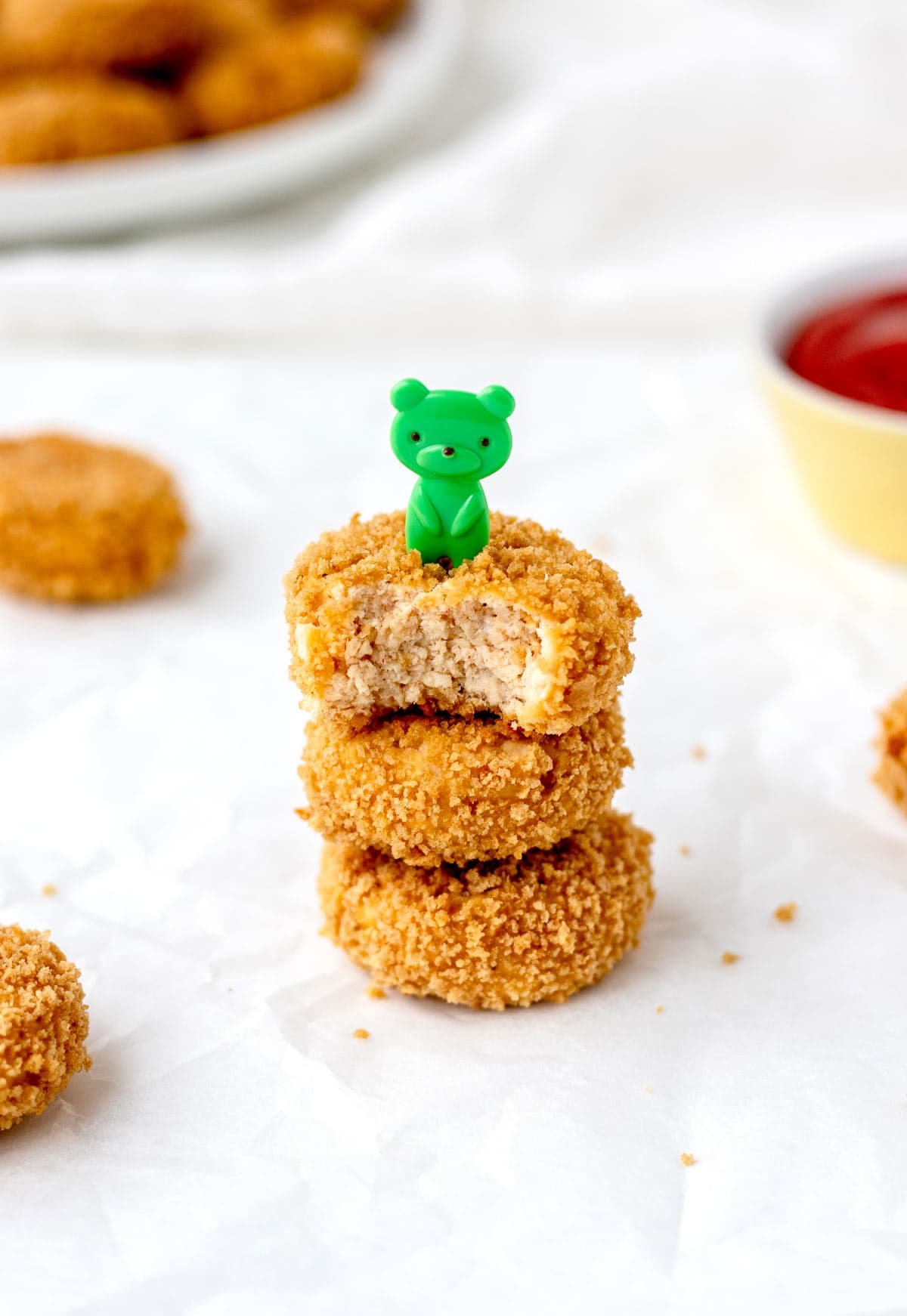 Baked cauliflower chicken nuggets stacked on top of one another on a plate with a green bear toothpick stuck in the top.