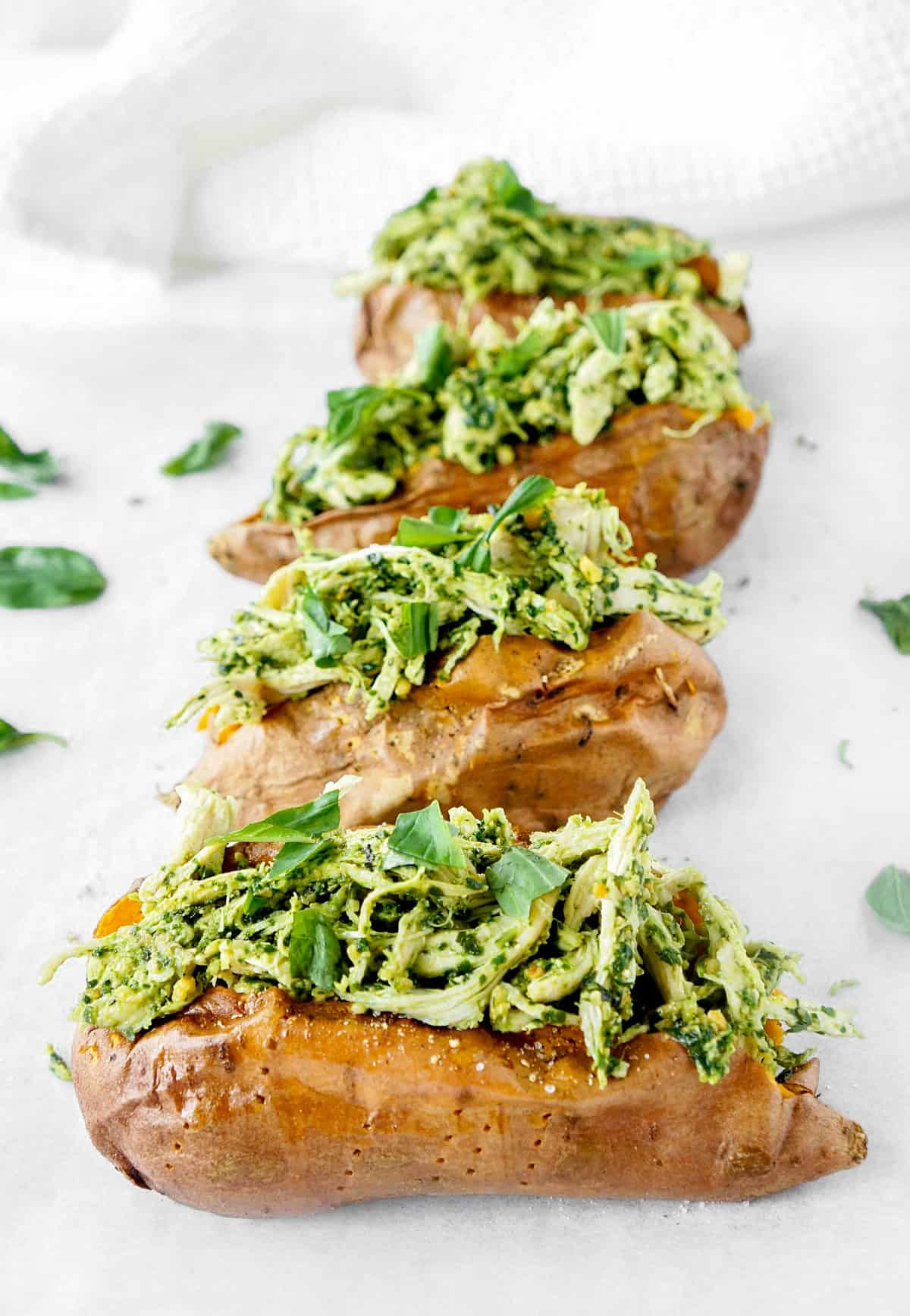 Pesto chicken stuffed sweet potatoes lined up on a white cutting board.