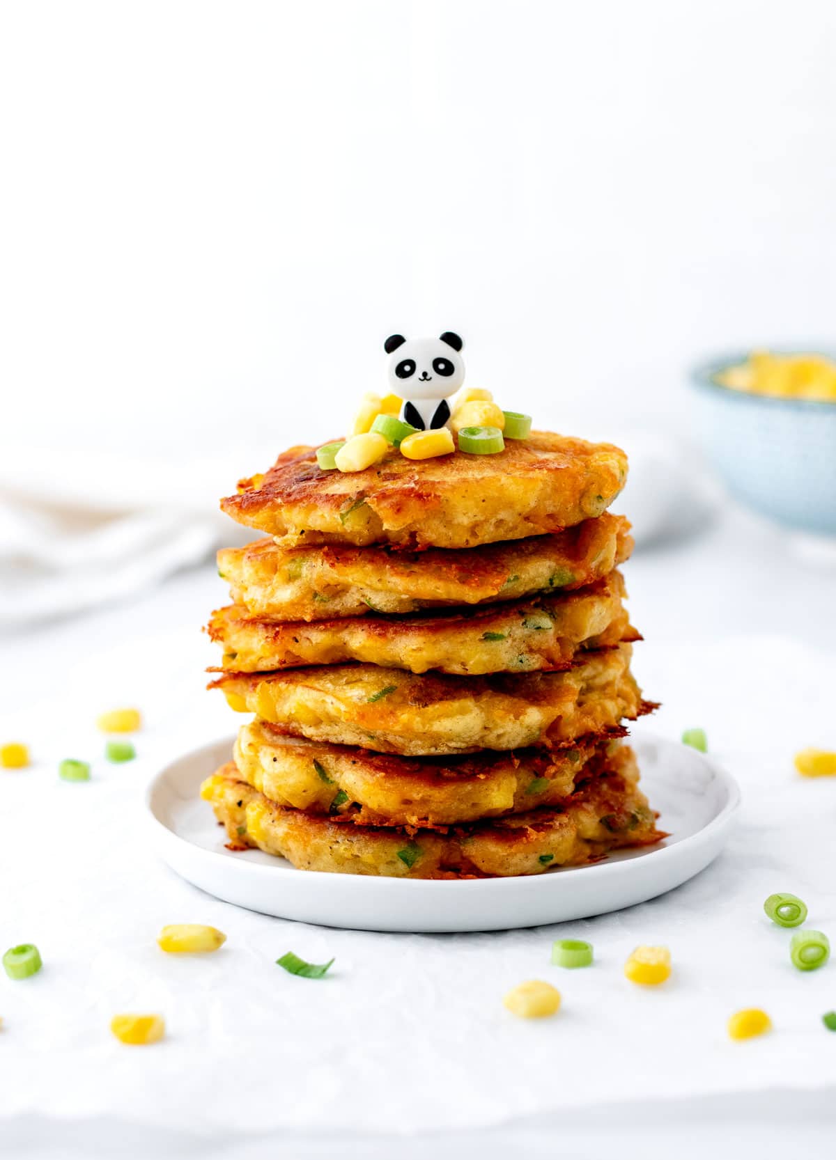 Cheesy corn fritters stacked on top of one another on a small white plate.