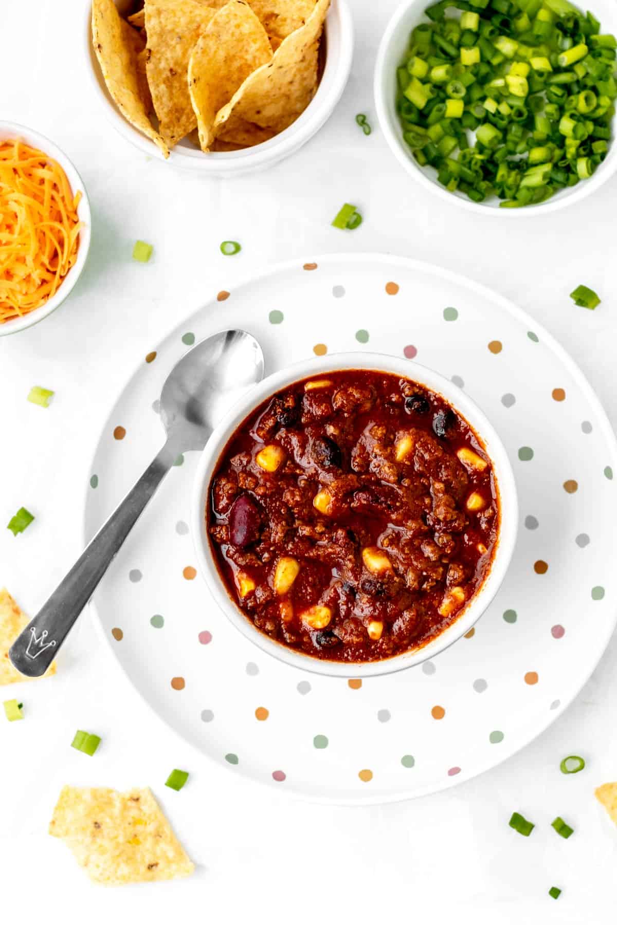 A small bowl of chili con carne and a spoon on a colorful polka dot plate.