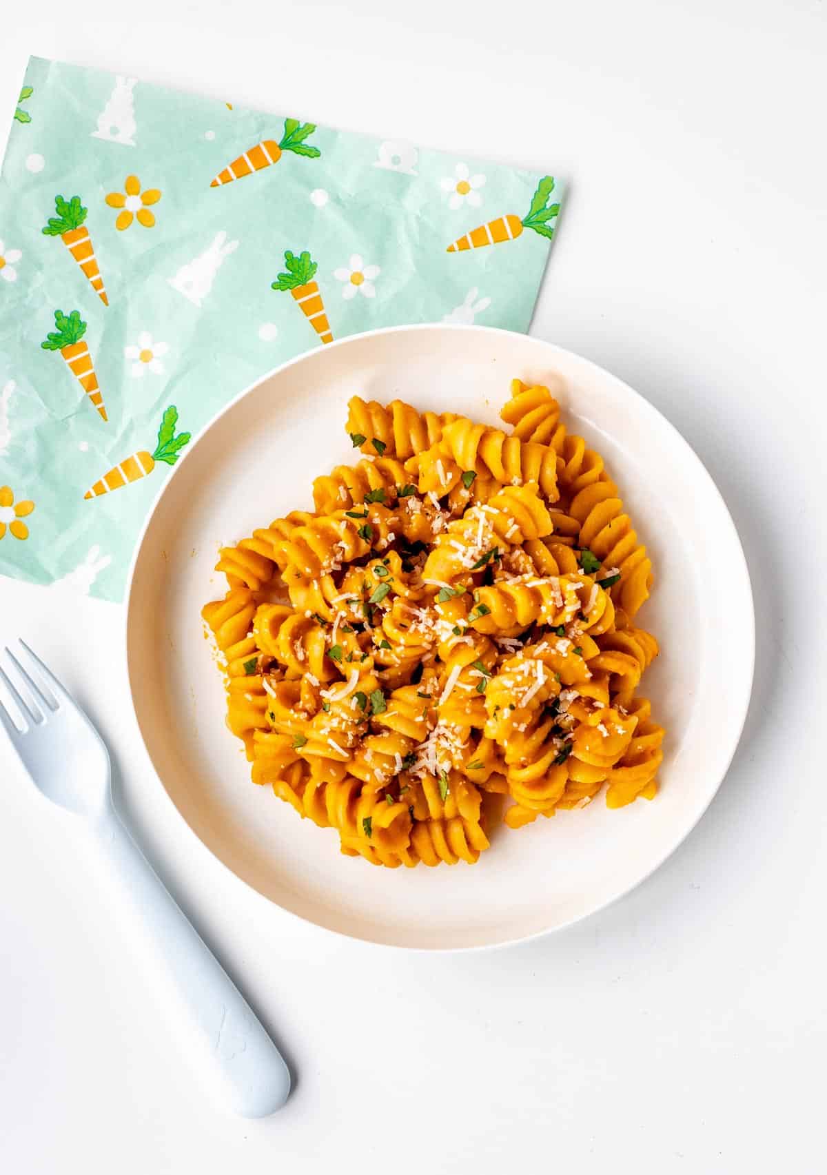 Roasted carrot pasta on a white plate next to a fork.