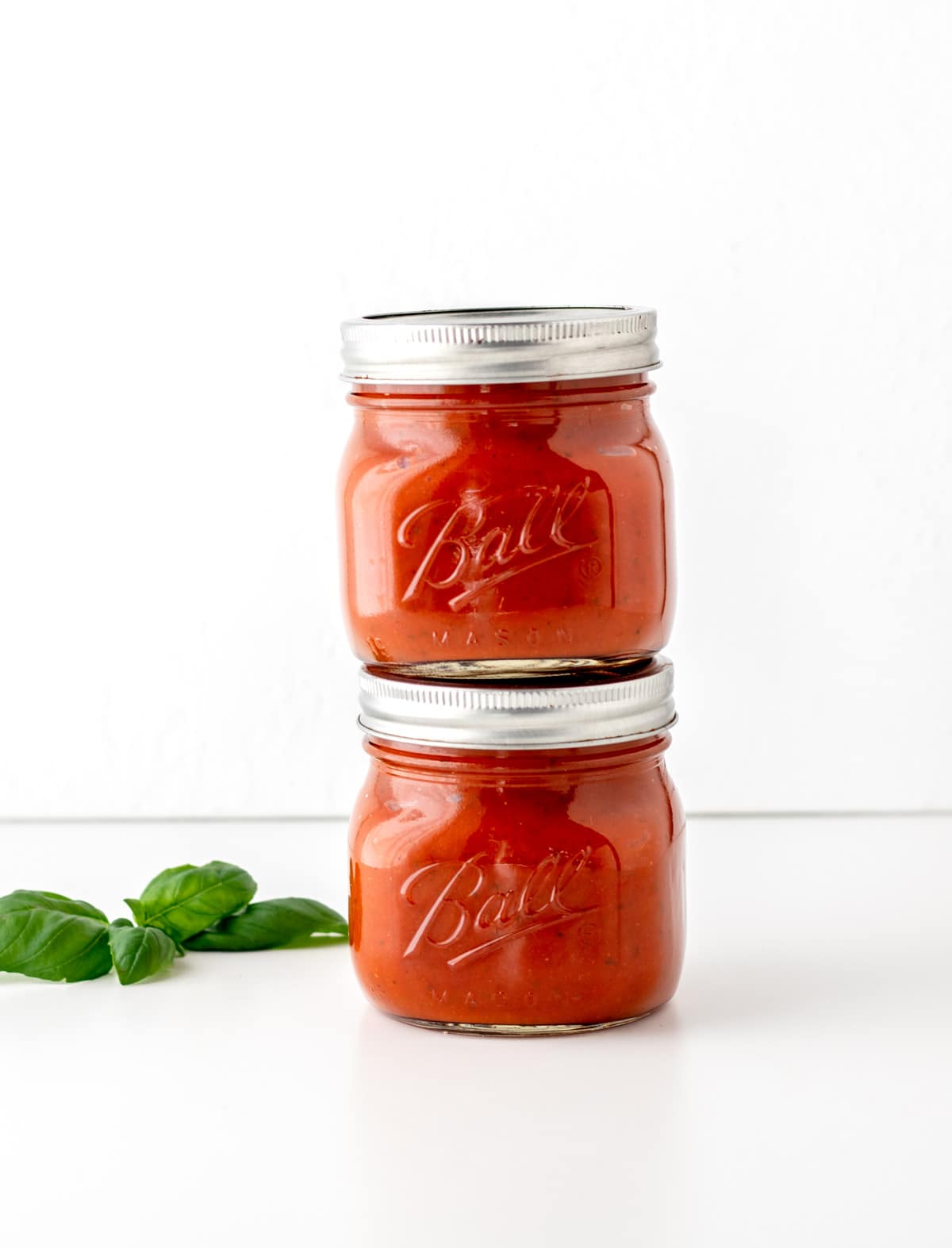 Two clear glass mason jars of hidden veggie pasta sauce stacked on top of one another.