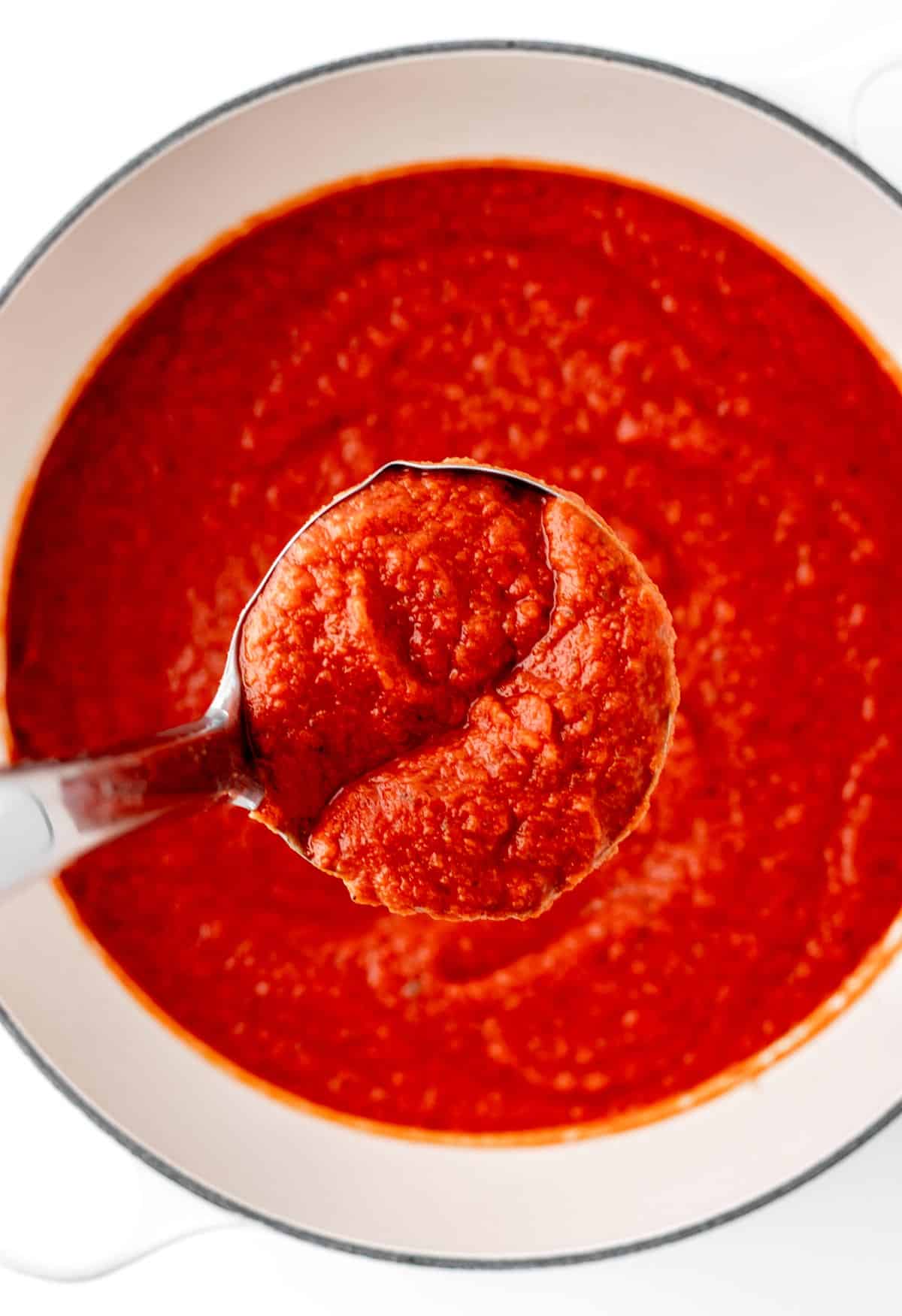 A ladle of pasta sauce with hidden vegetables with a large pot of it in the background.