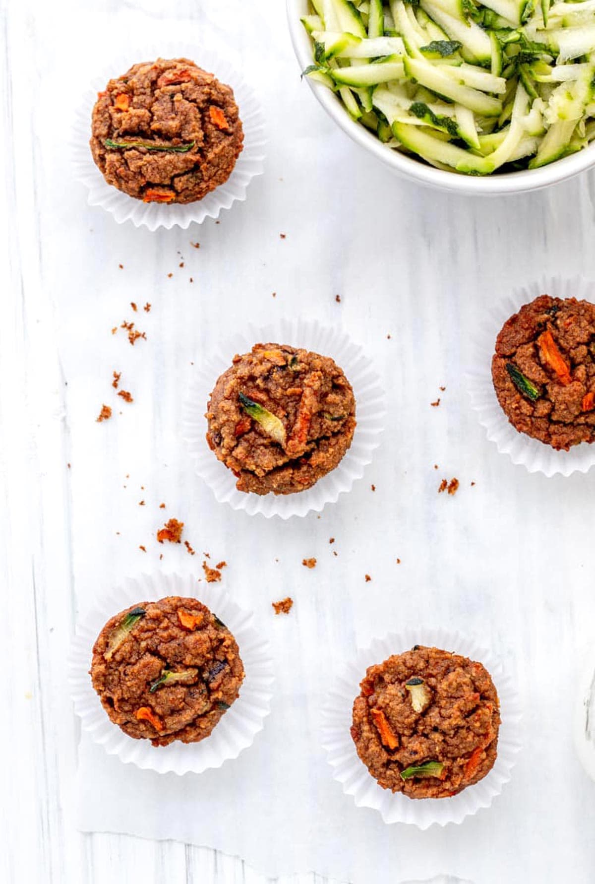 Carrot zucchini muffins spread out on a cooling rack lined with parchment paper.