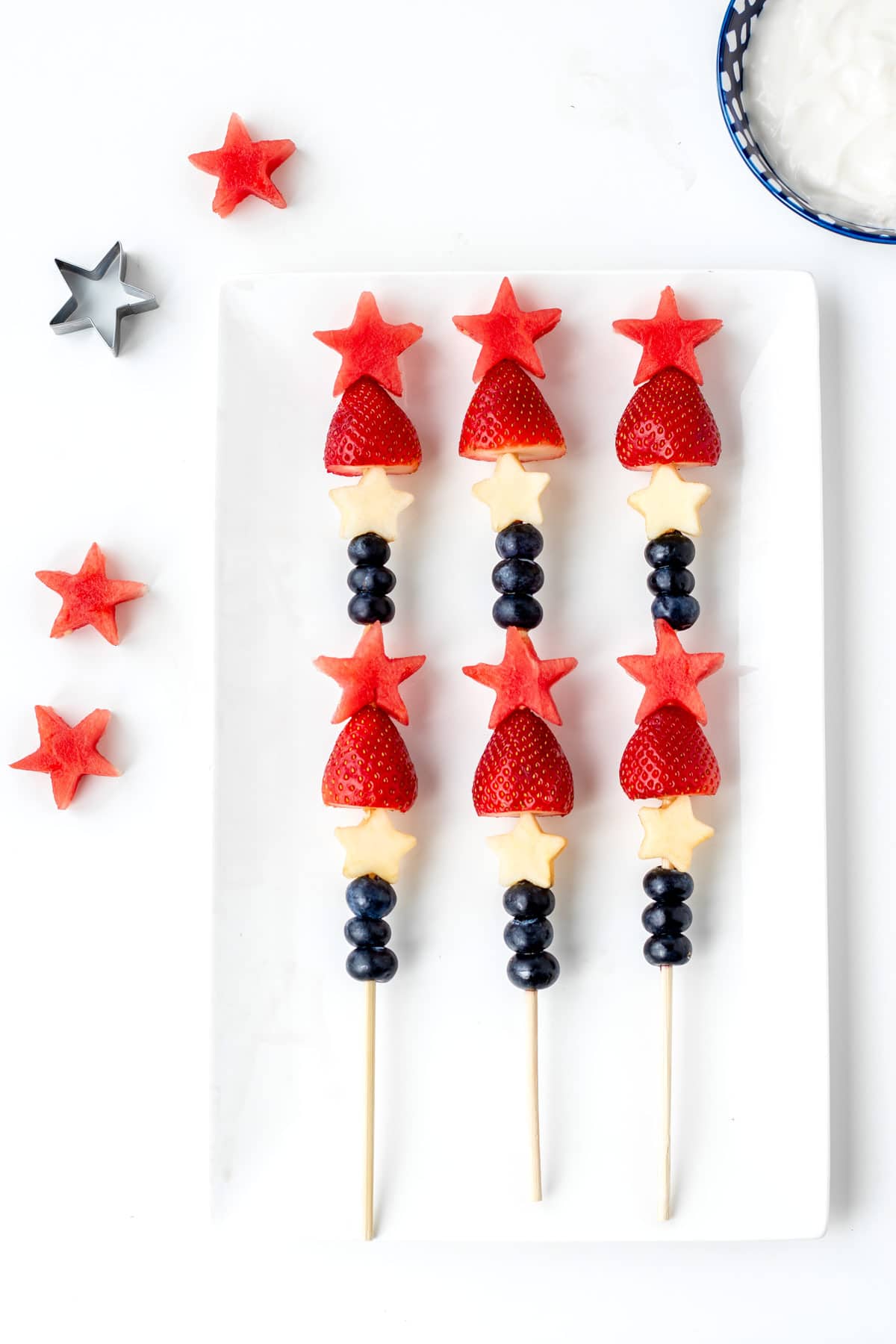 Red, white and blue fruit kabobs on a white platter.