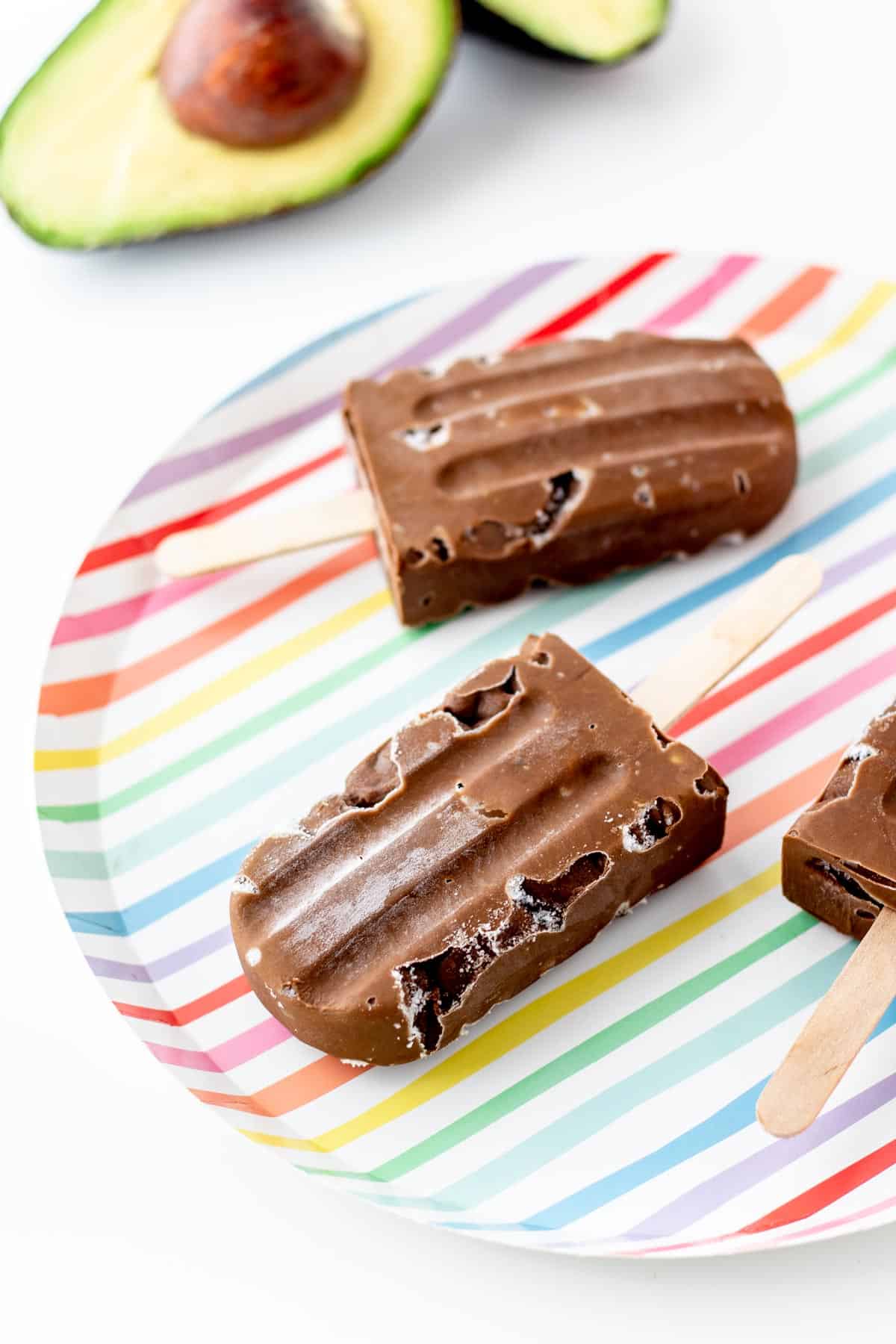 Avocado fudgesicles on a colorful striped plate.