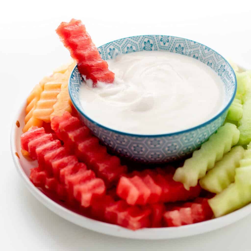 Fruit fries on a plate with one dipped in a bowl of yogurt dip.