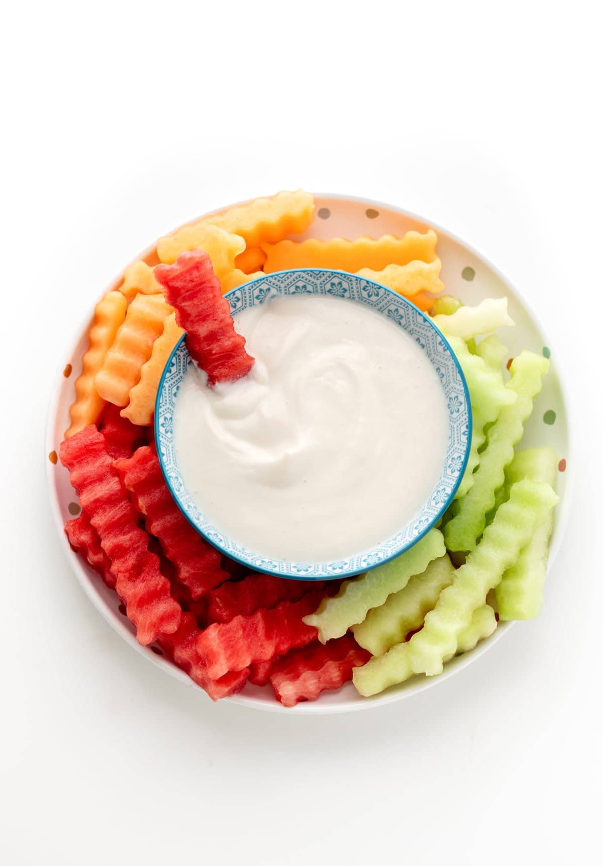Fruit fries on a plate with a bowl of yogurt dip in the middle.