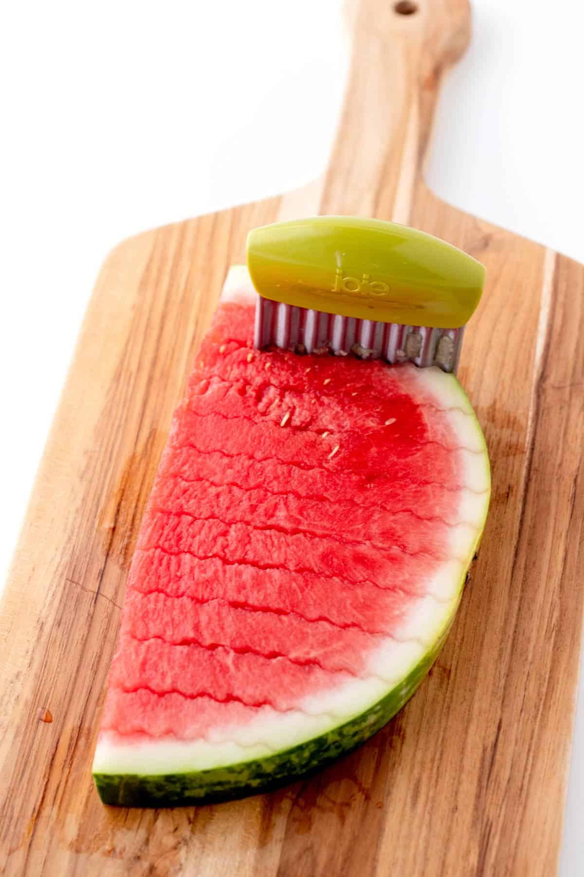 Using a crinkle cutter to make watermelon fries on a cutting board.