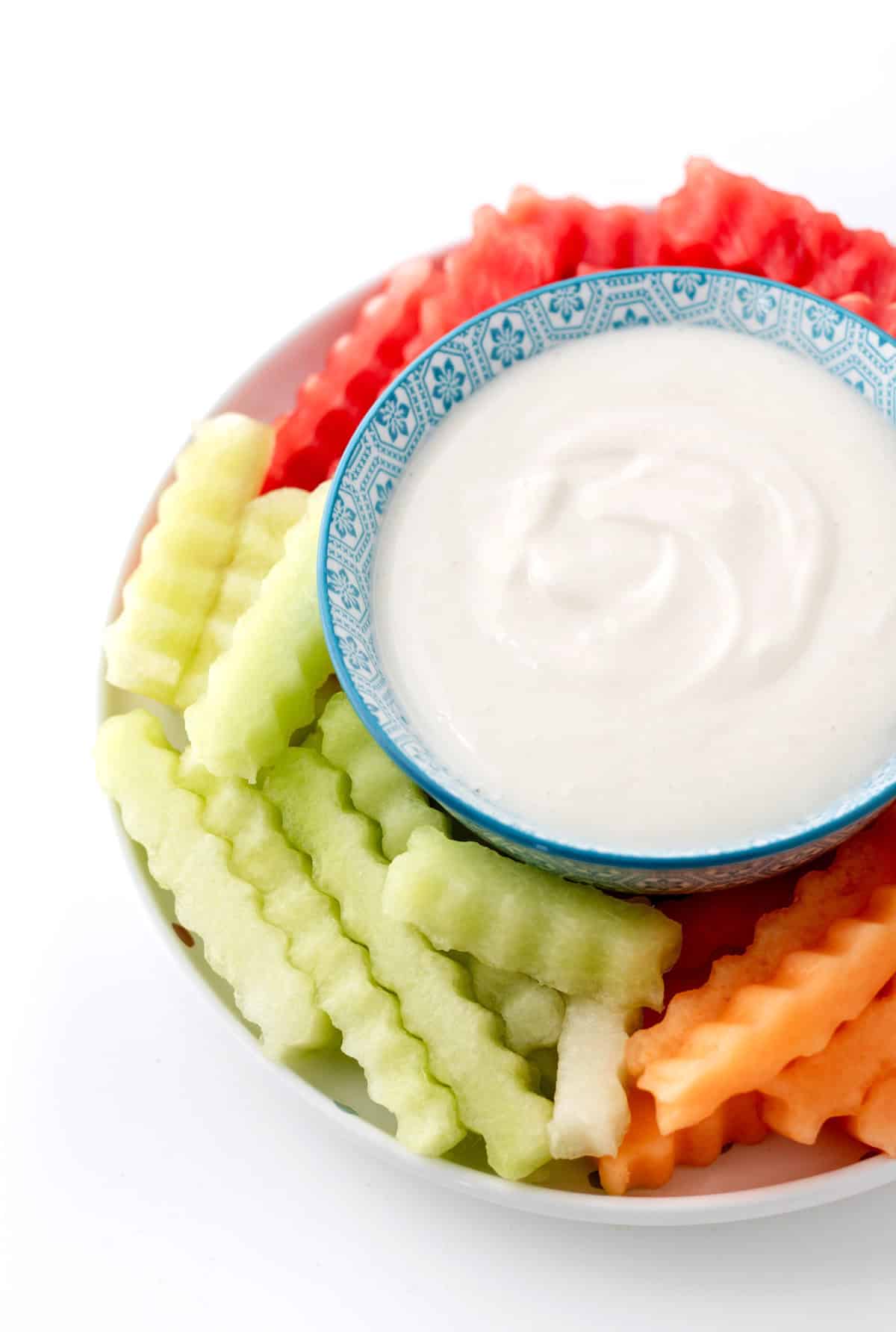 A close-up of fruit fries on a platter with a bowl of Greek yogurt dip in the middle.