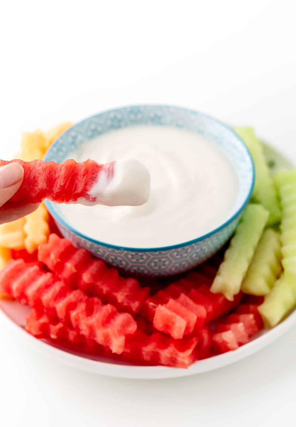 Someone dipping a watermelon fry into a bowl of yogurt dip.